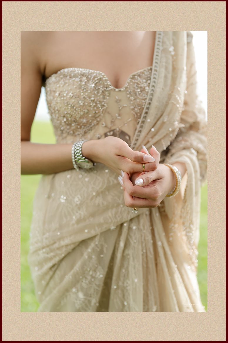 Close-up of bride in beige sequined saree with pearl bracelet and delicate rings on manicured hands.