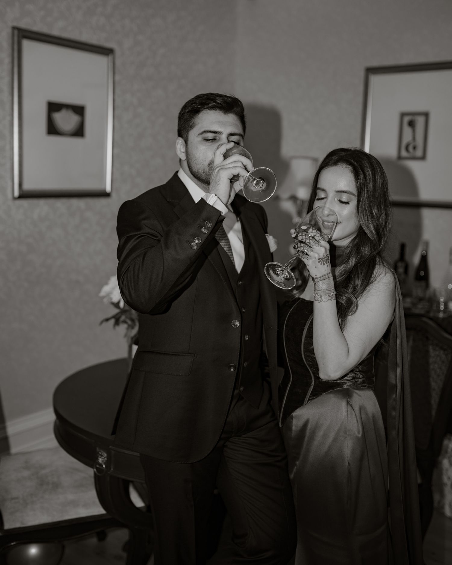 Couple in formal attire sipping champagne in black and white wedding photo.