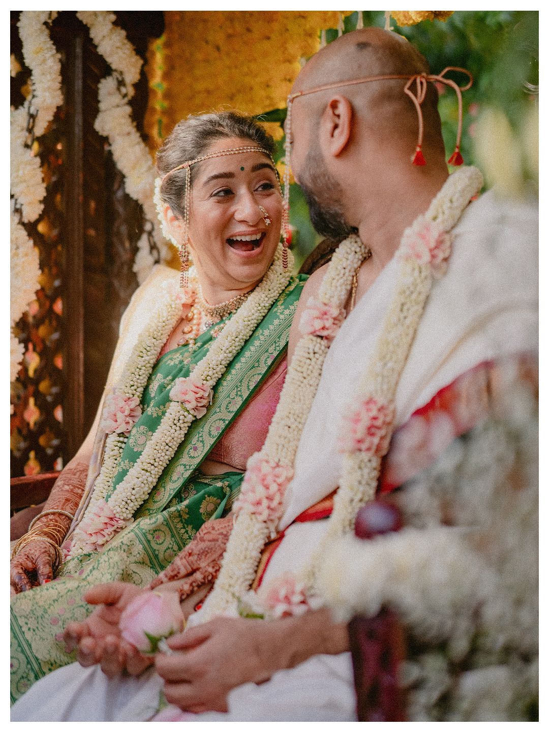 Indian bride in green silk saree laughing joyfully with groom during traditional wedding ceremony.