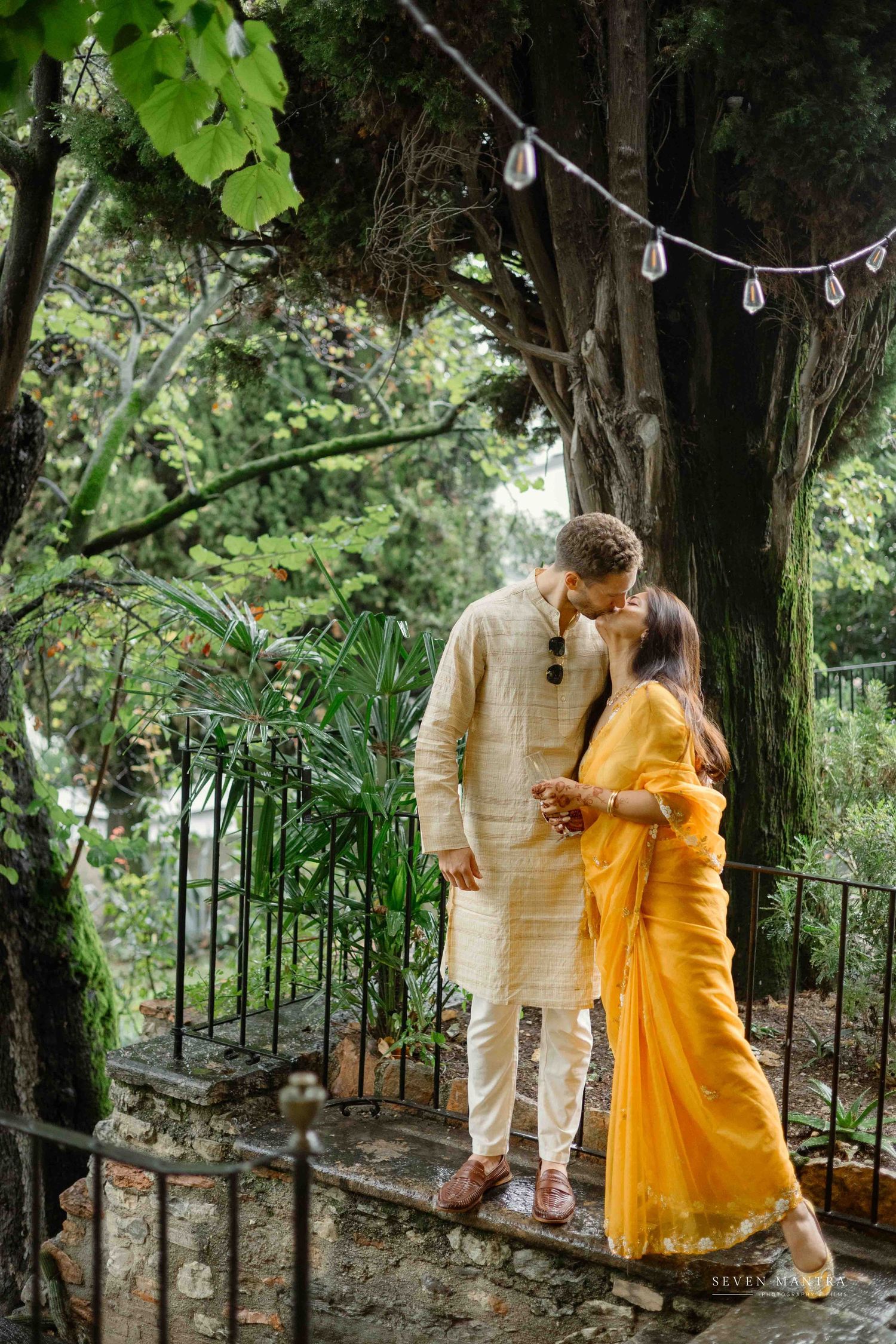 Couple in traditional Indian attire sharing a romantic moment in a lush garden setting.