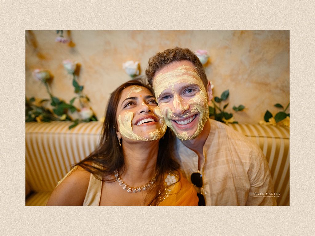 Smiling couple with turmeric paste on their faces during a traditional Indian haldi wedding ceremony.