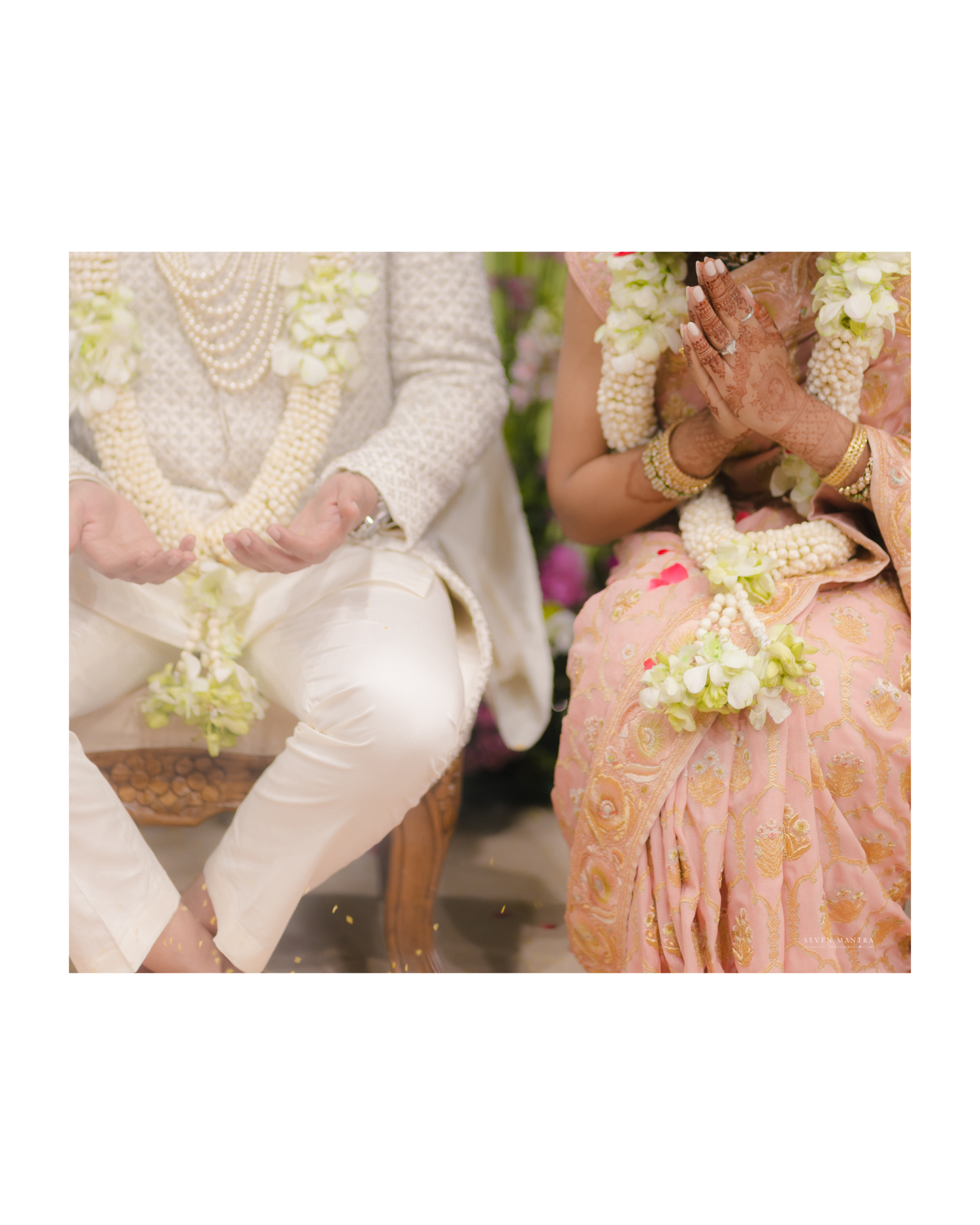 Close-up of Indian bride and groom holding hands with jasmine garlands during traditional wedding ceremony.