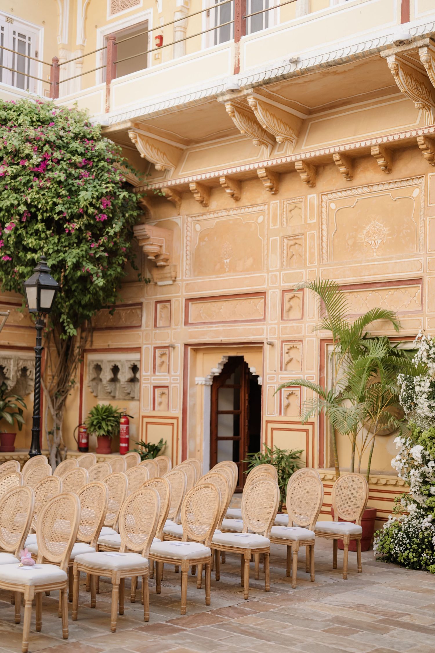 Rows of elegant wooden chairs arranged in ornate Indian palace courtyard for outdoor wedding ceremony.