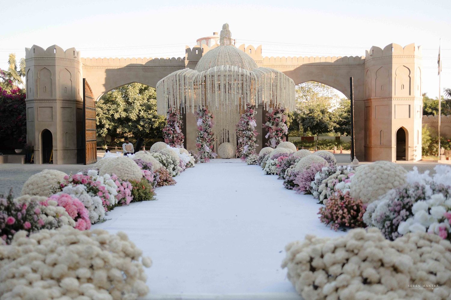 Stunning Indian wedding mandap with white floral aisle lined with pink and white chrysanthemums.
