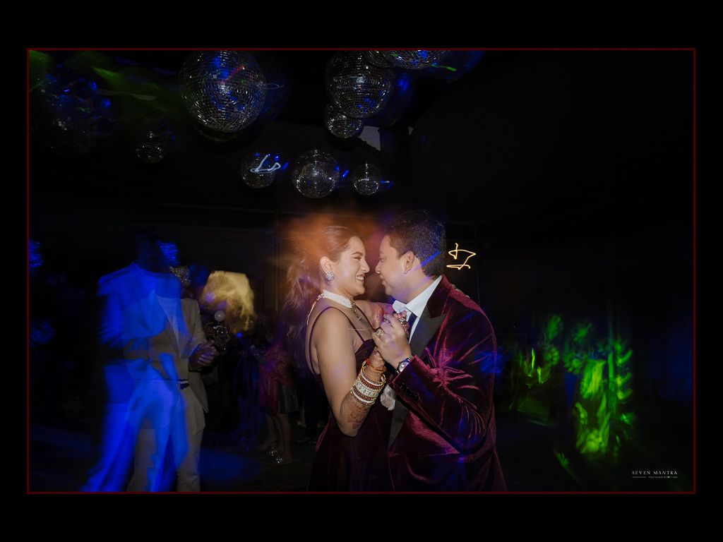 Couple shares a romantic dance moment under colorful lights at an Indian wedding reception celebration.