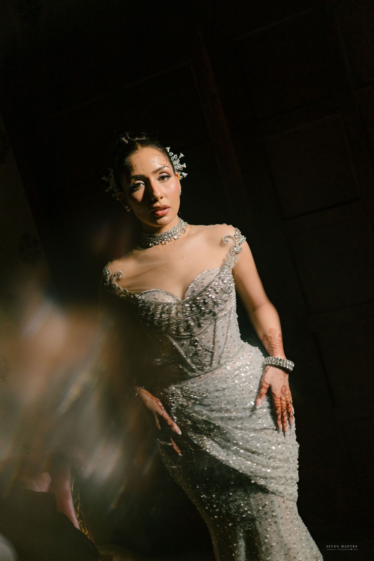 Bride in a stunning silver beaded mermaid gown with sheer details and crystal hair accessories poses dramatically.