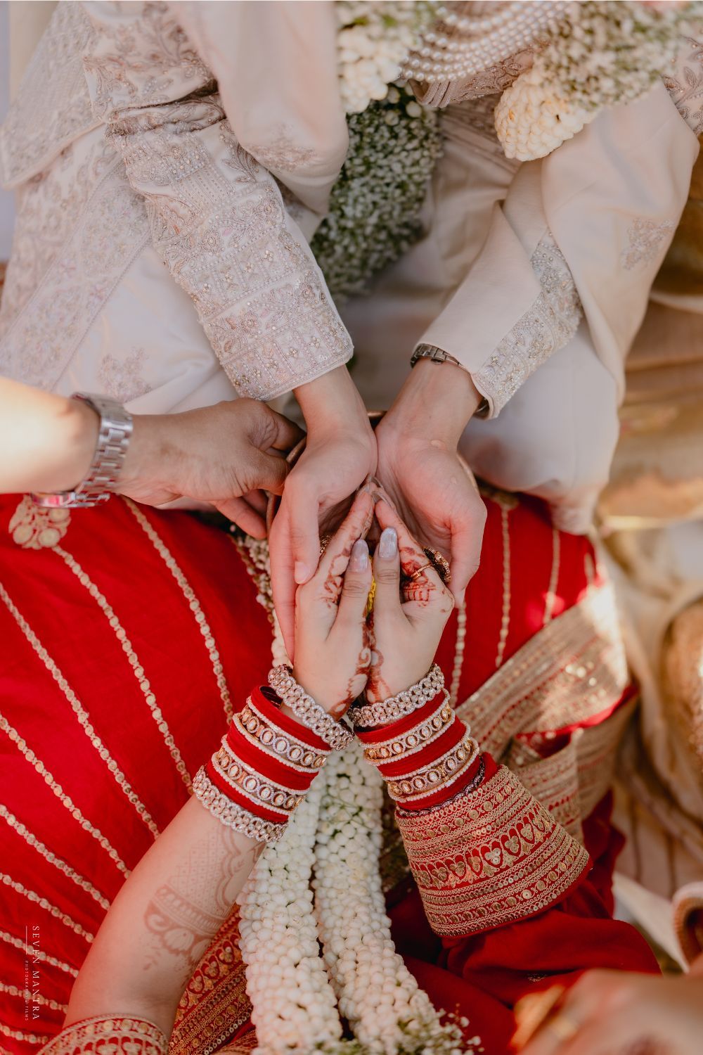 Close-up of Indian bride and groom's hands adorned with bangles and mehndi during wedding ritual.