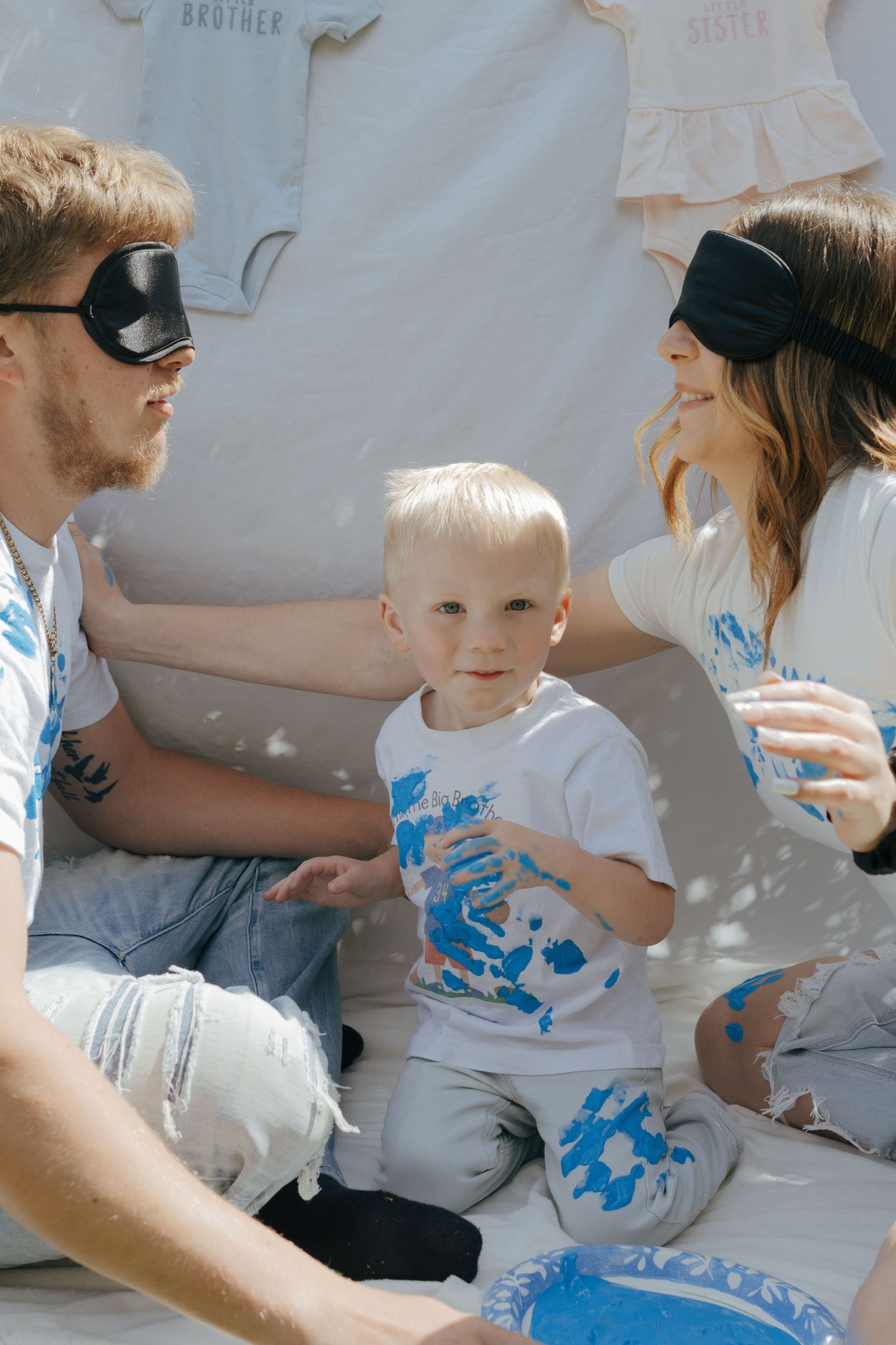 Family with toddler covered in blue paint at gender reveal party outdoors.