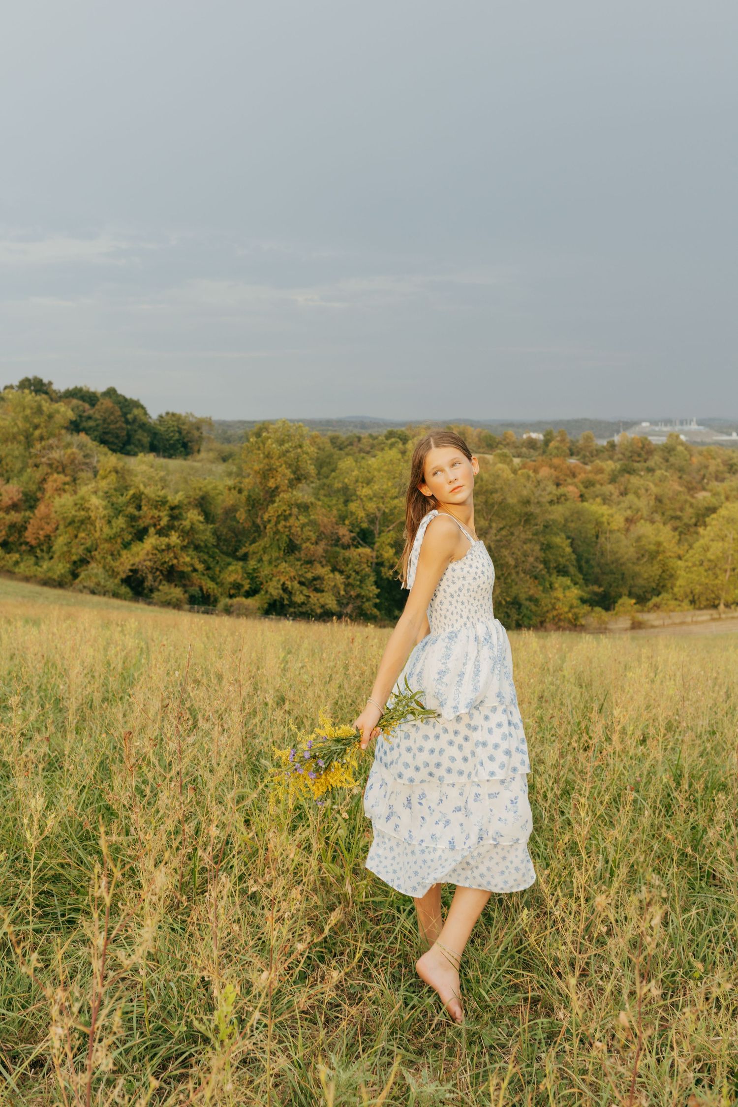 Young woman in a floral sundress holding wildflowers in a golden meadow Pittsburgh senior session