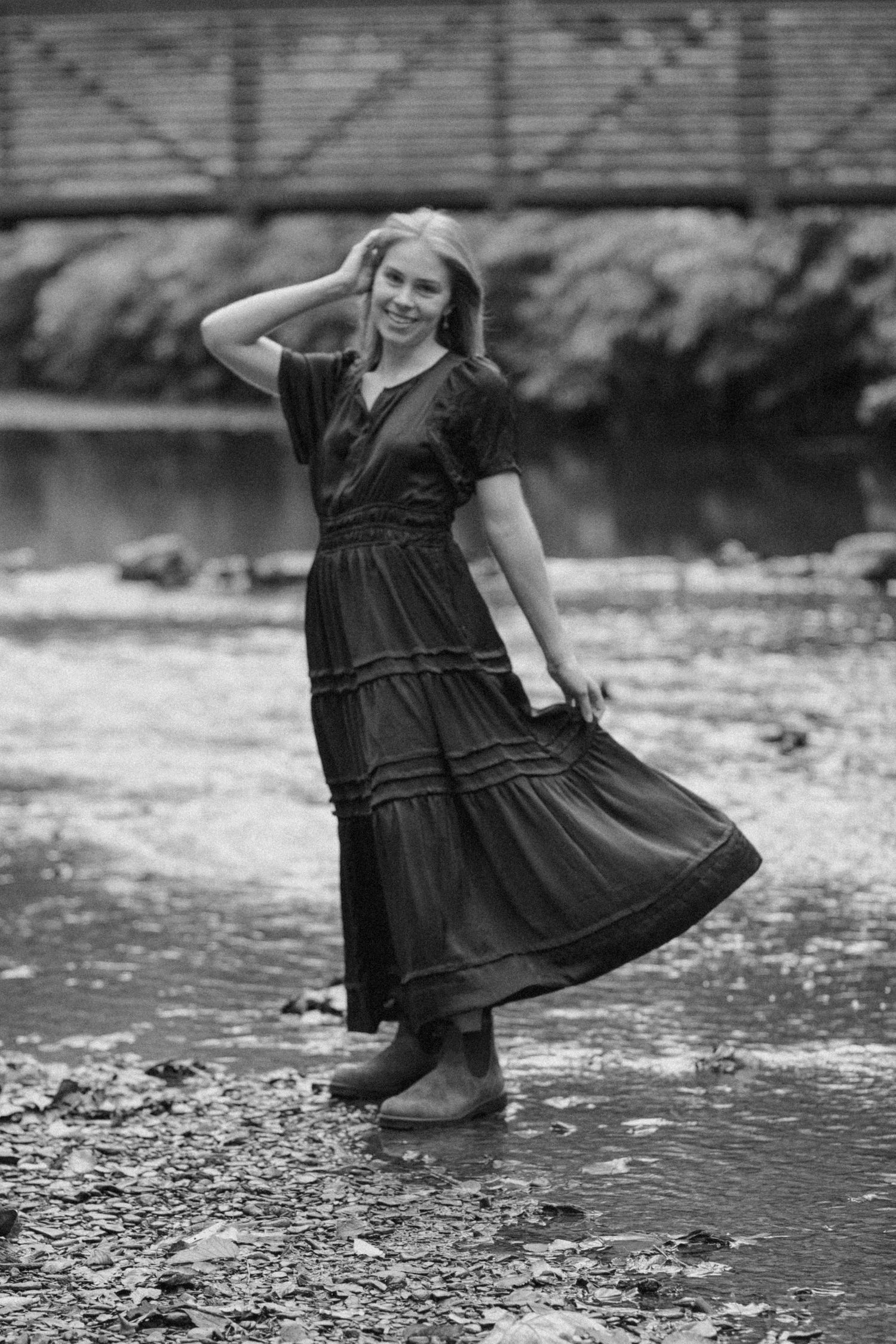 Black and white photo of a woman in a maxi dress wading in a creek.