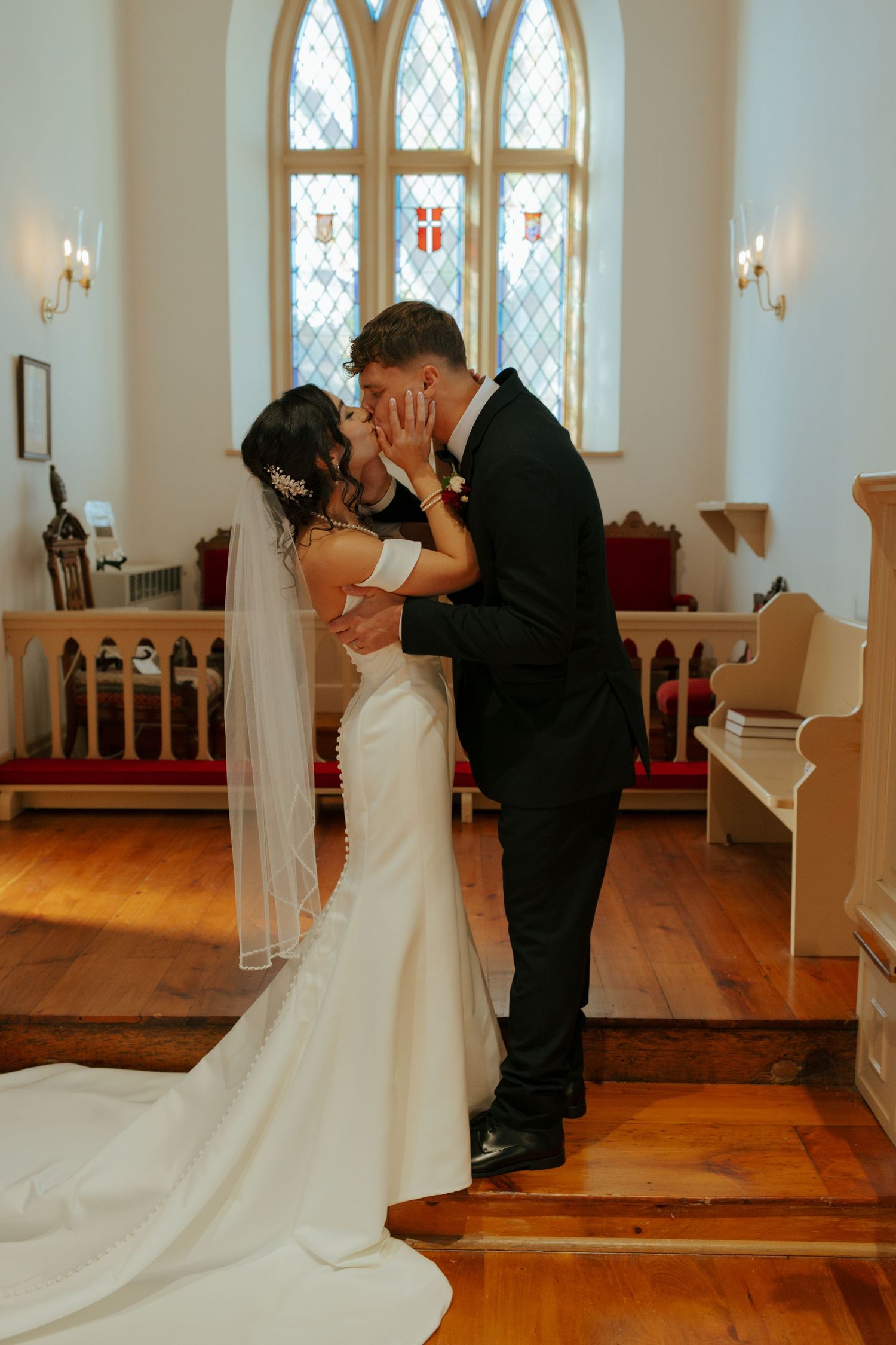 Newlyweds sharing their first kiss inside a charming chapel with stained glass windows.