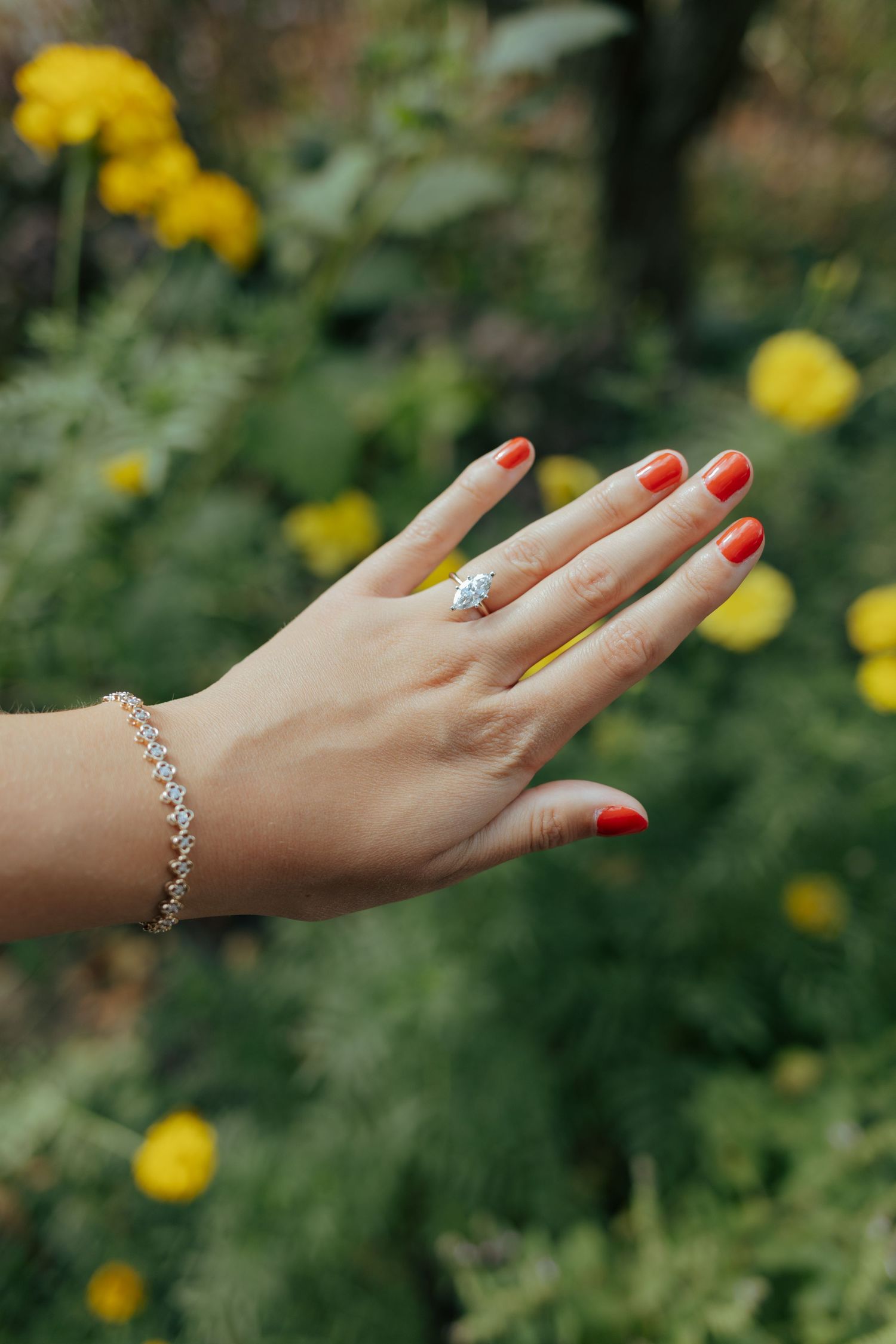Close-up of a woman's hand with red nails wearing a diamond engagement ring and tennis bracelet.