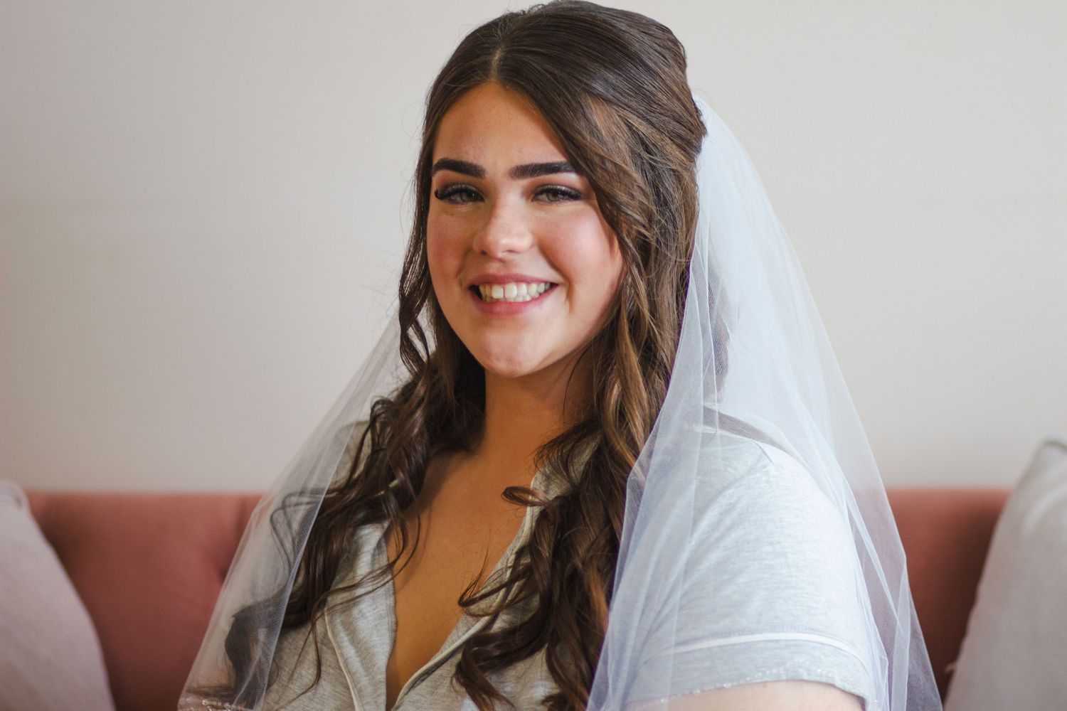 Smiling bride wearing a white veil with long wavy brown hair on her wedding day.