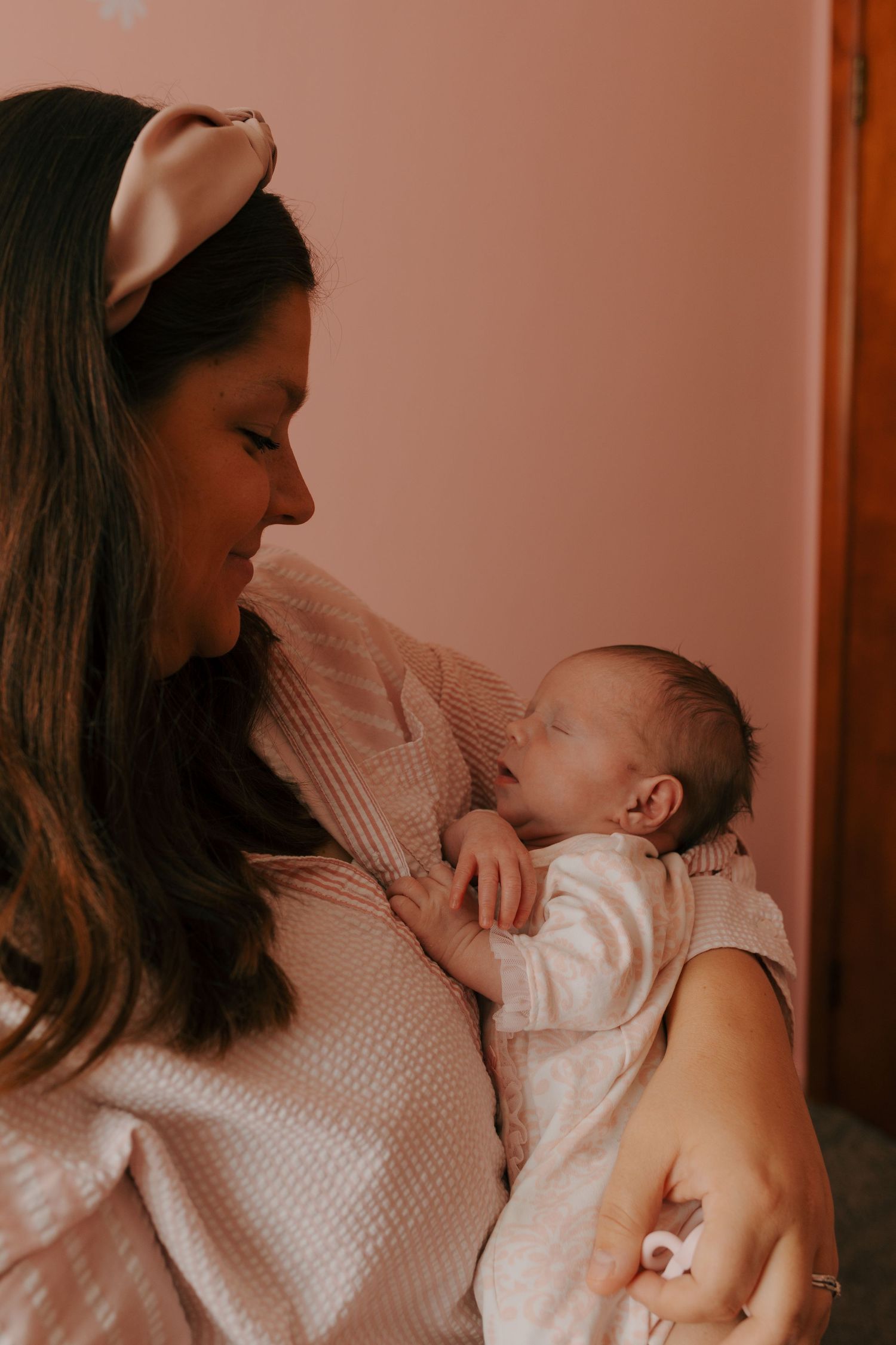 Loving mother with satin headband gazing down at her sleeping newborn baby in her arms.