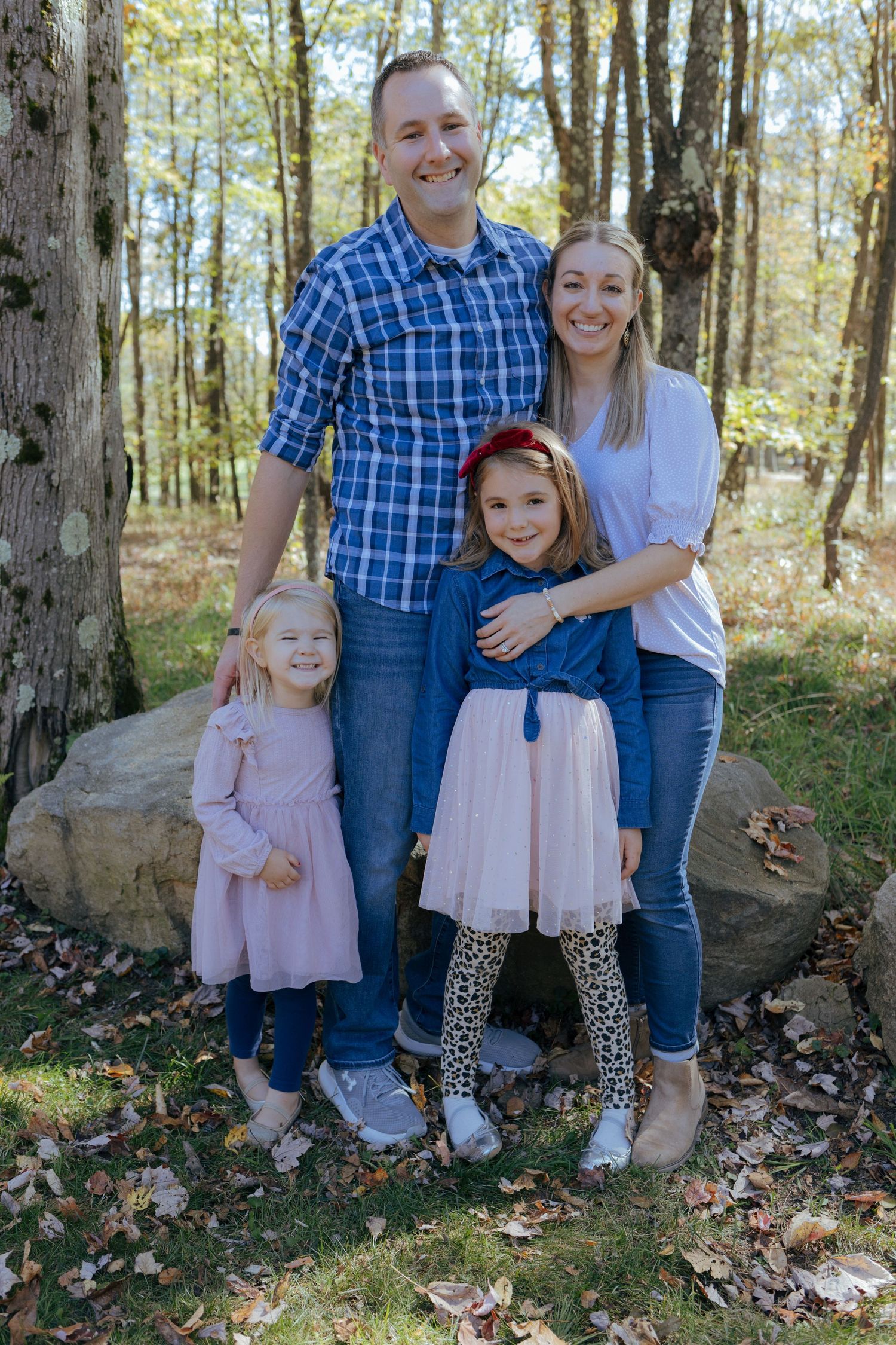 Smiling family of four poses together on rock in colorful autumn forest setting in Pittsburgh