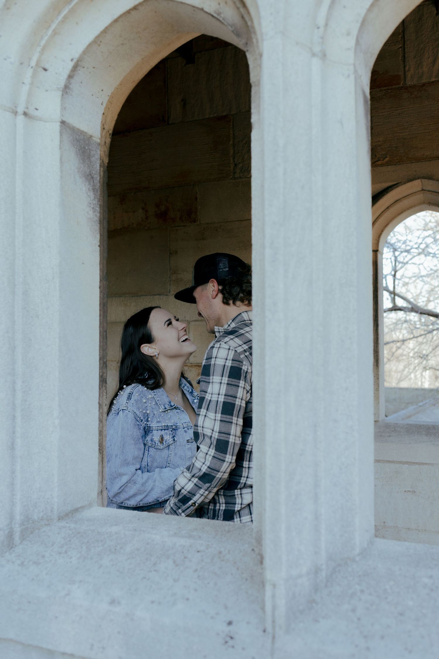 Happy couple shares romantic moment laughing together under stone arched architectural alcove.