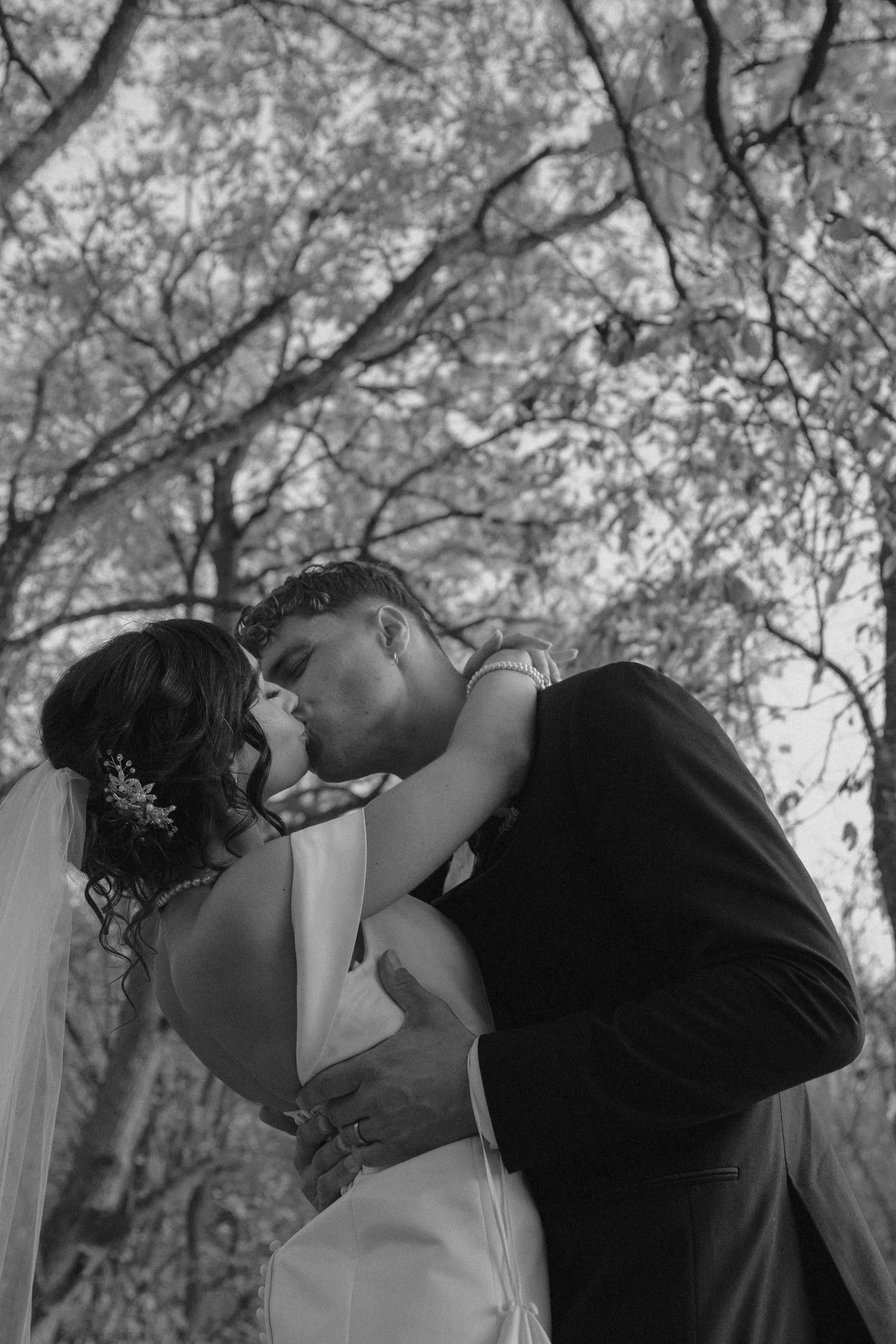 Black and white photo of a bride and groom sharing a romantic kiss under trees at a wedding in Pittsburgh