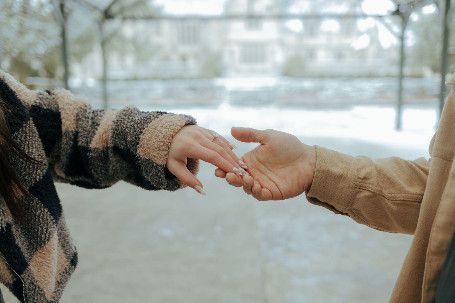 Close-up of couple gently reaching for each other's hands in a snowy winter outdoor setting.