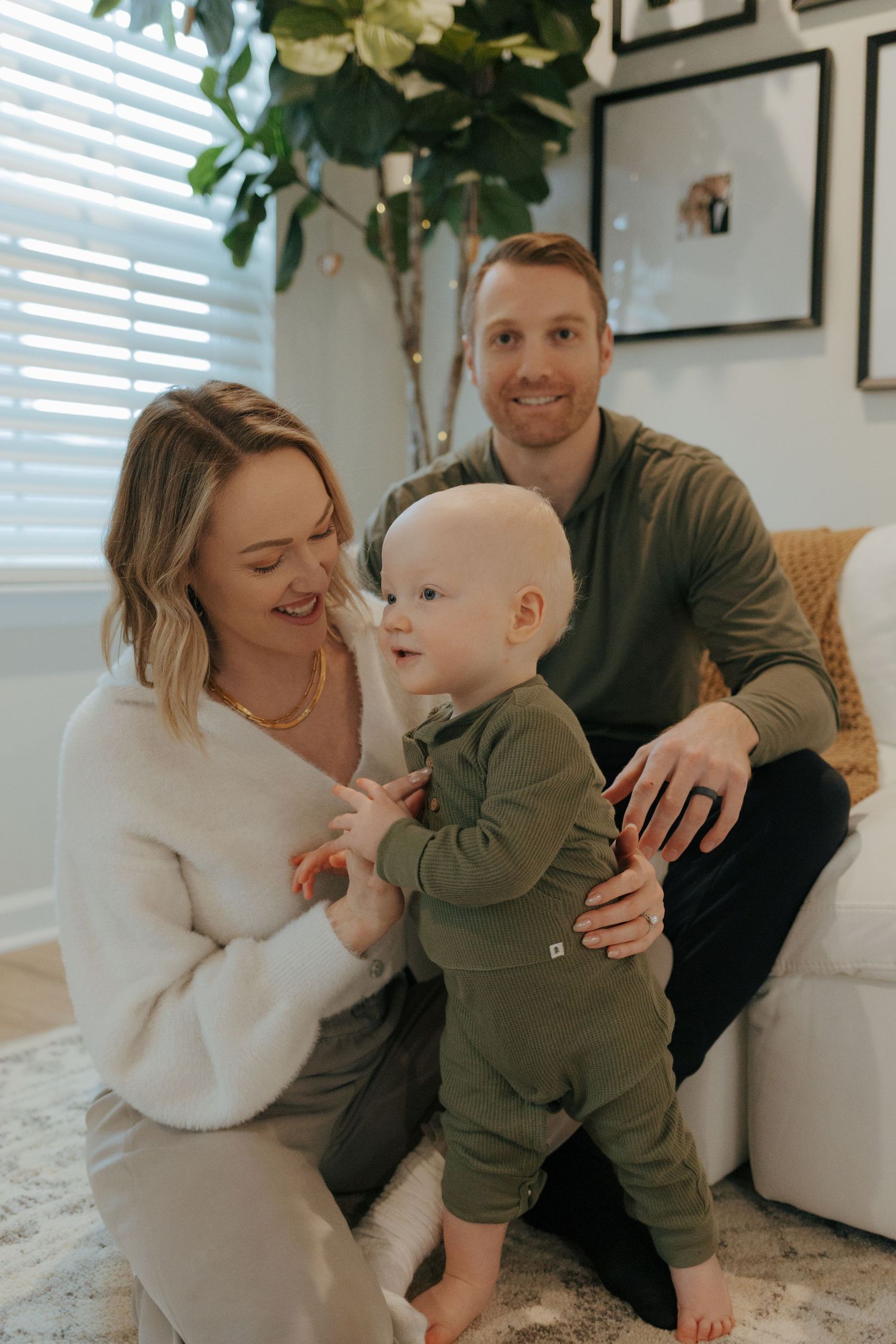 A young family with their baby boy standing between them in a cozy decorated living room.