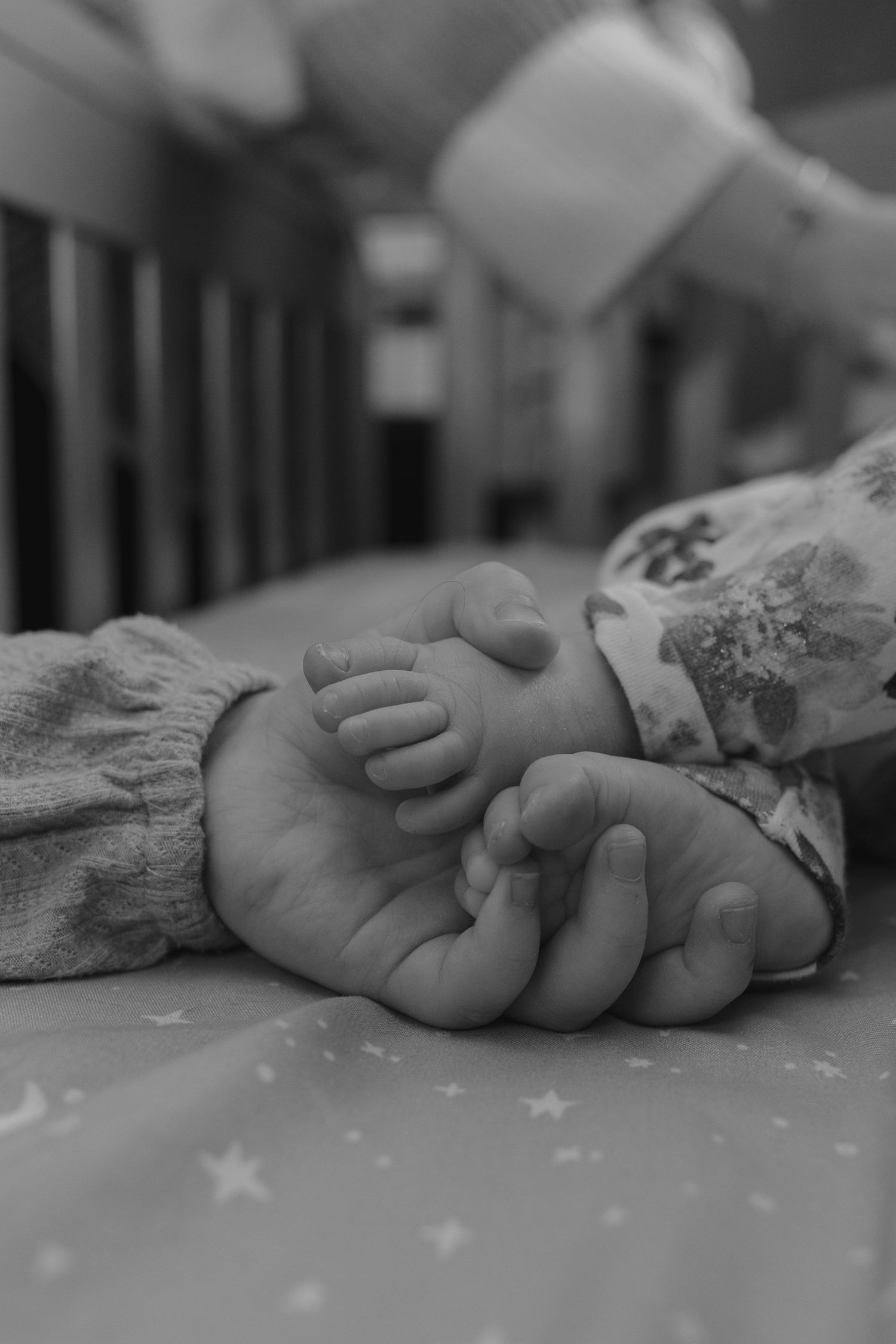 Black and white close-up of a newborn baby's tiny feet held gently in small hands.