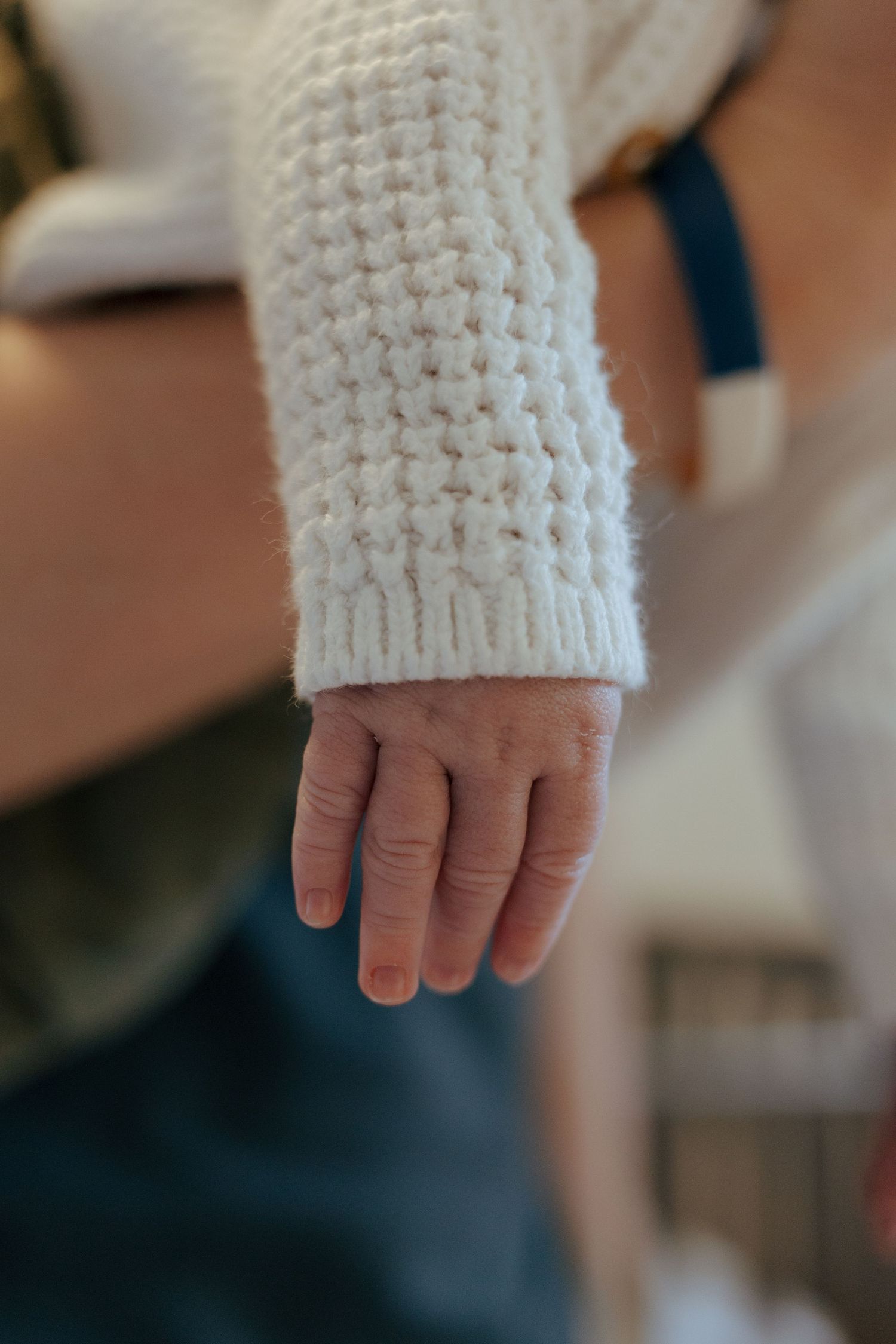 Newborn baby's small hand dangling from white knit sweater sleeve.