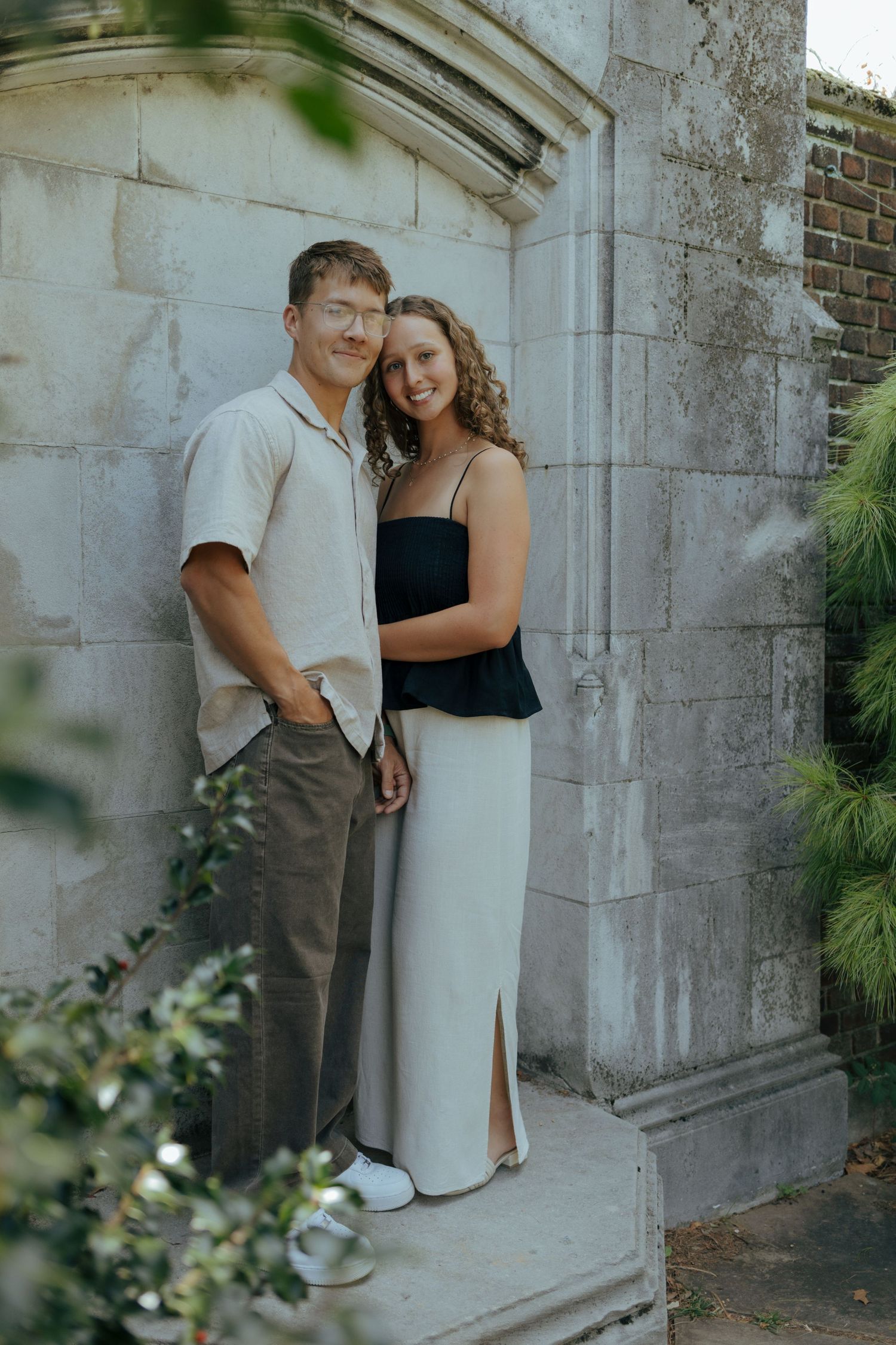 Smiling couple posing together against an aged stone wall with ivy and architectural details.
