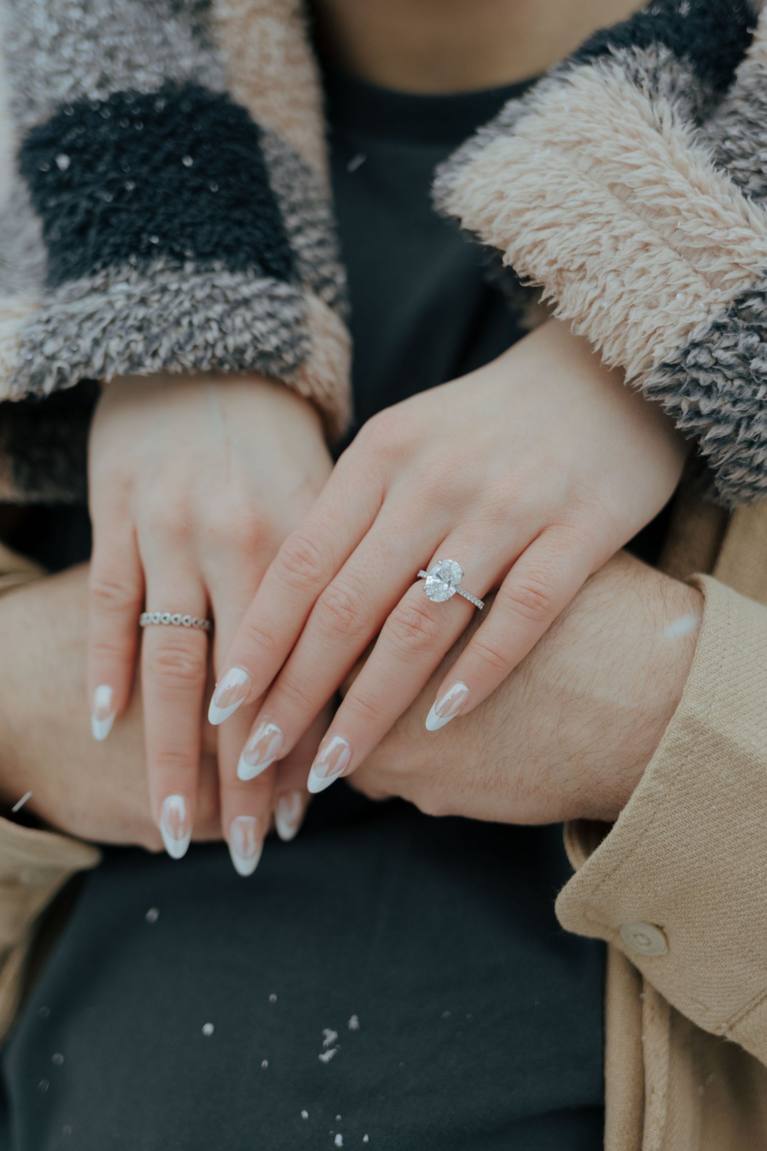Close-up of engaged couple's hands showing a solitaire diamond engagement ring in winter.