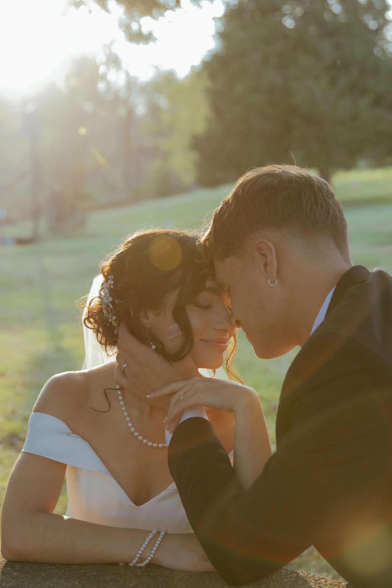 Bride and groom sharing a tender forehead touch moment in golden sunset light outdoors on their wedding day.