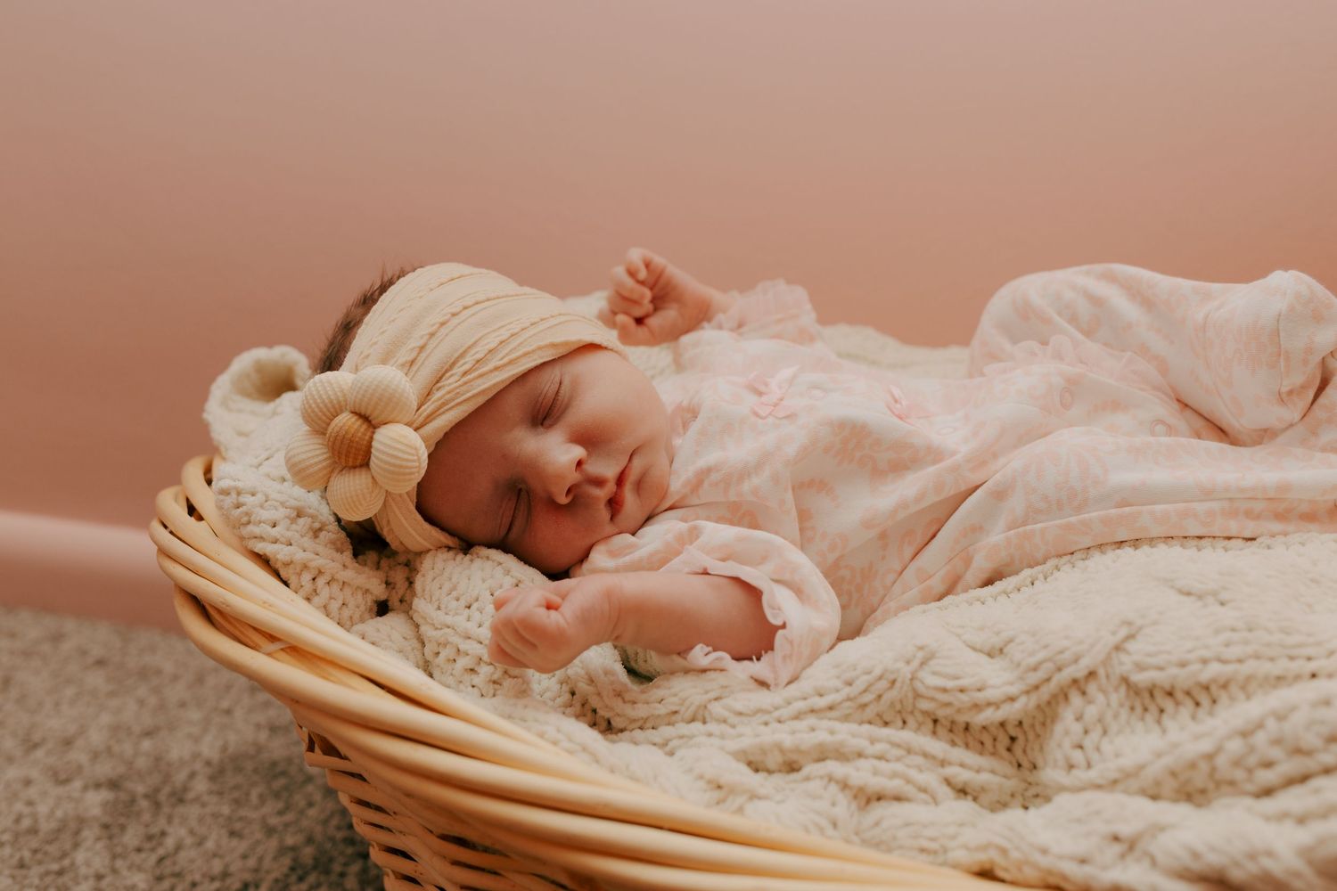 Peaceful newborn baby girl sleeping in wicker basket wrapped in white knit blanket with toy.