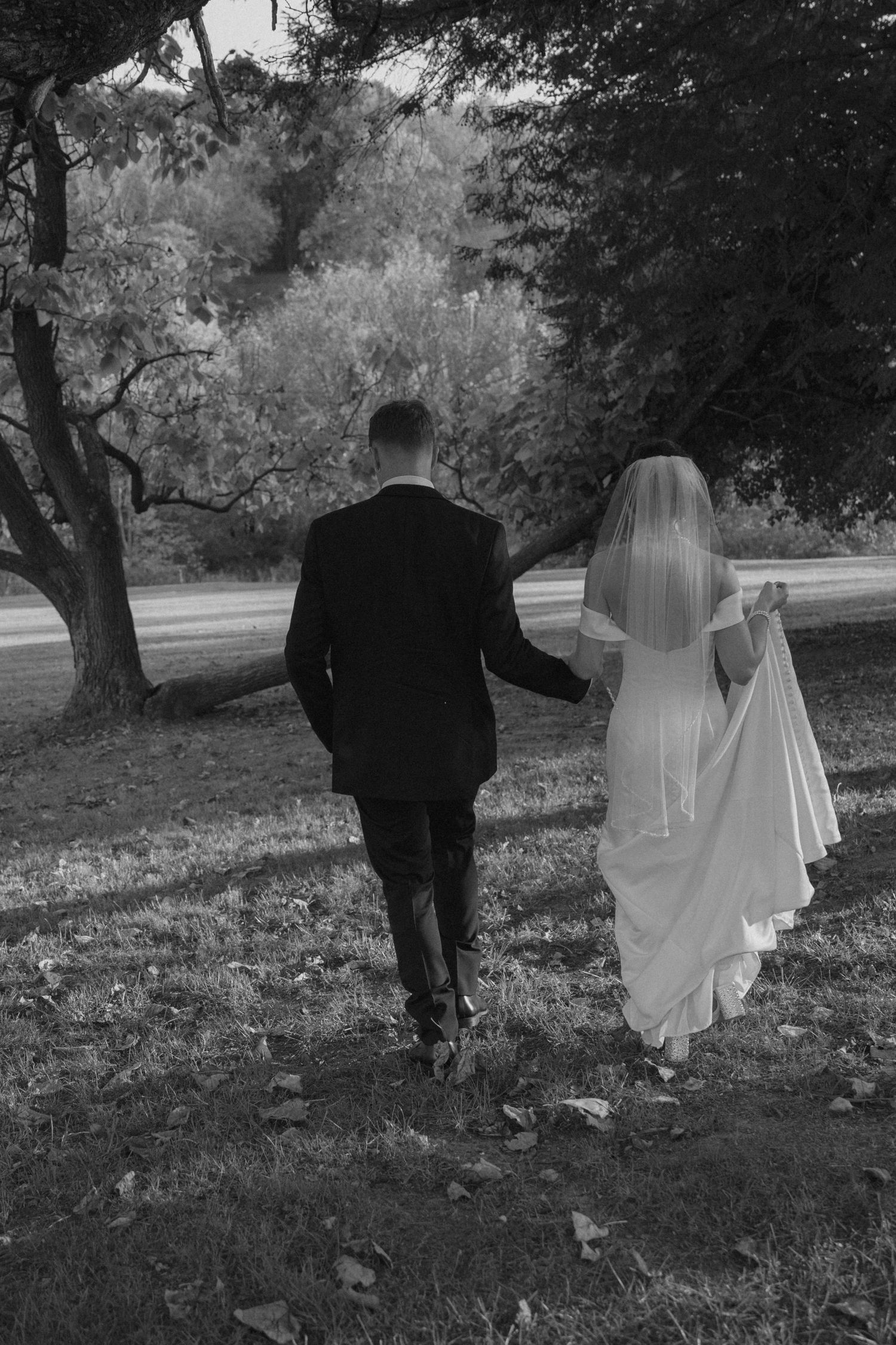 Black and white wedding photo of bride in veil and groom in suit walking together through a scenic park. Pittsburgh wedding photography.