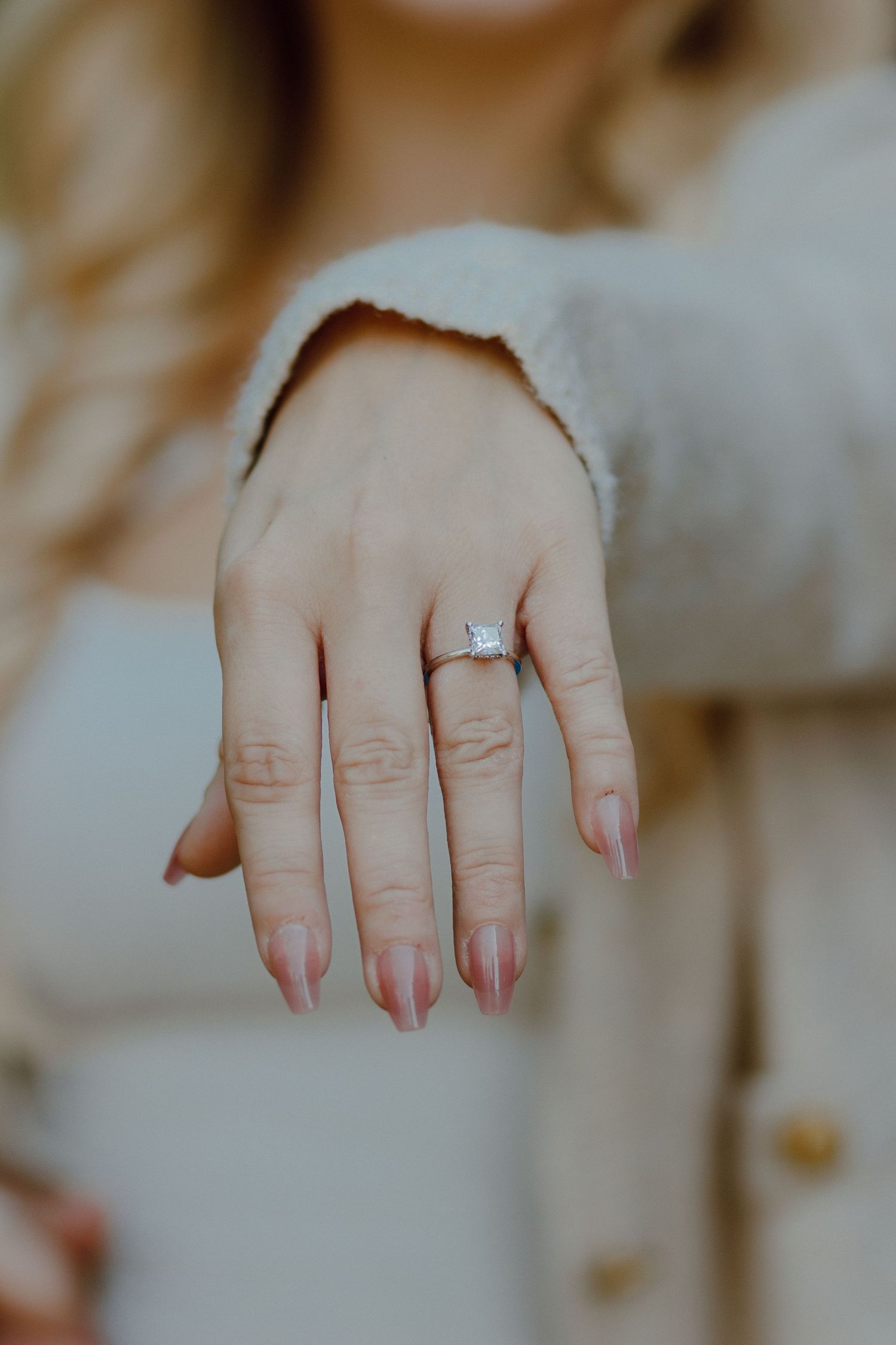 Woman extending her hand to display a stunning square-cut diamond solitaire engagement ring with manicured nails.