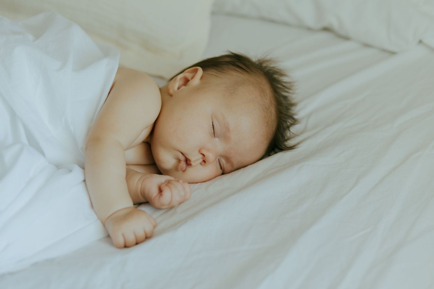 Newborn baby sleeping peacefully on soft white bedding.