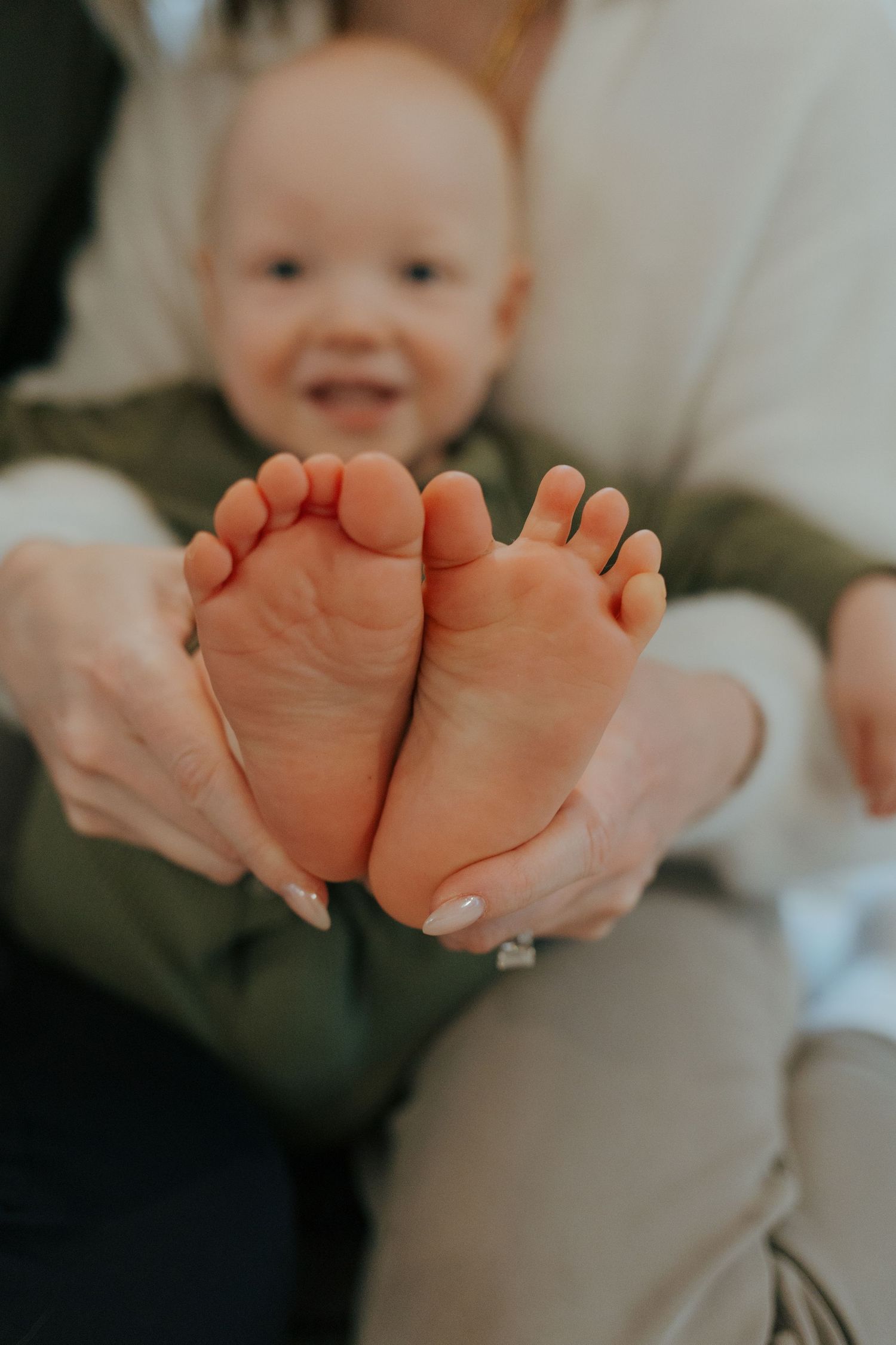 Close-up of a laughing baby's tiny feet held gently by a parent's hands.