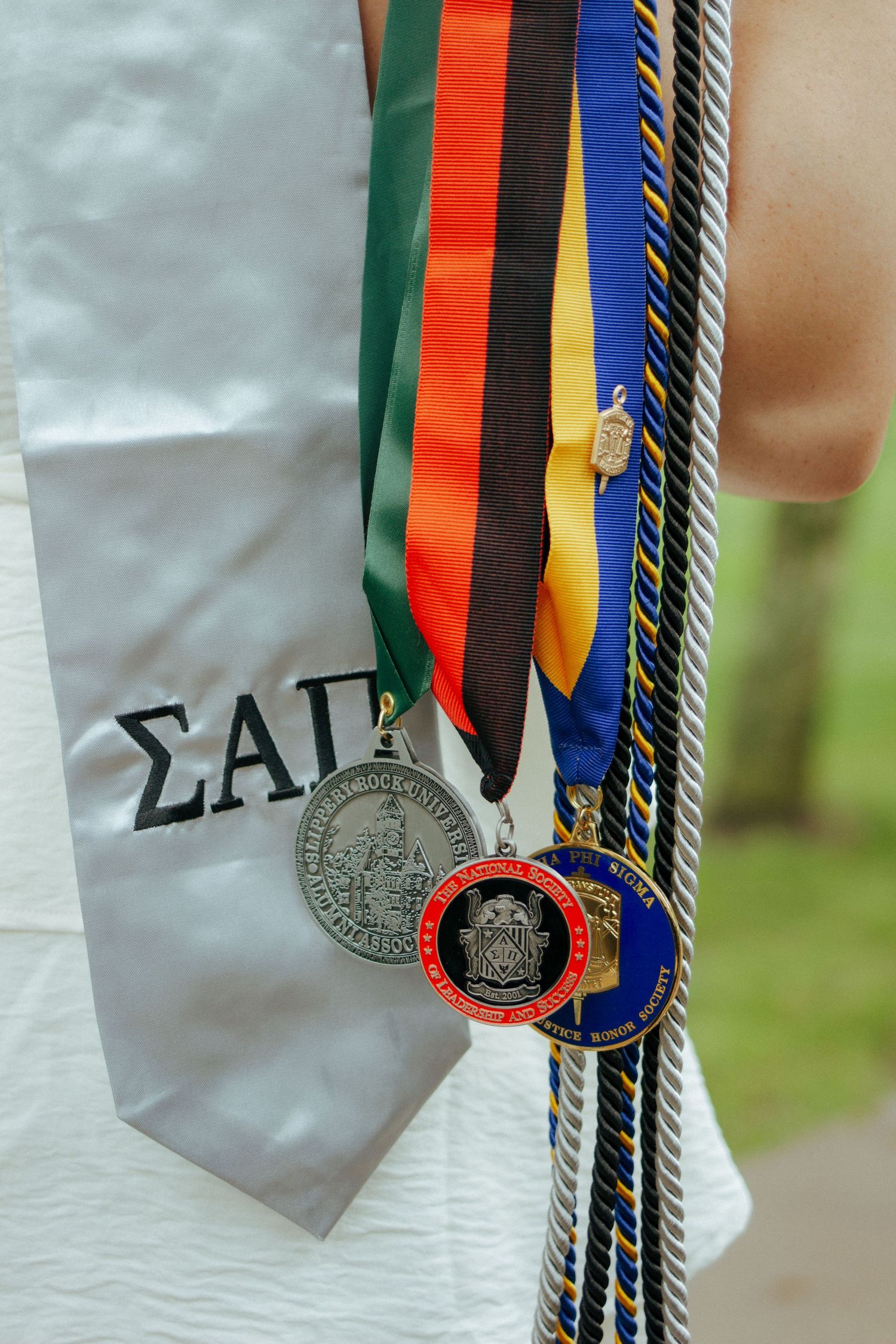 Close-up of graduation medals, honor cords, and Sigma Alpha Pi stole worn by graduate.