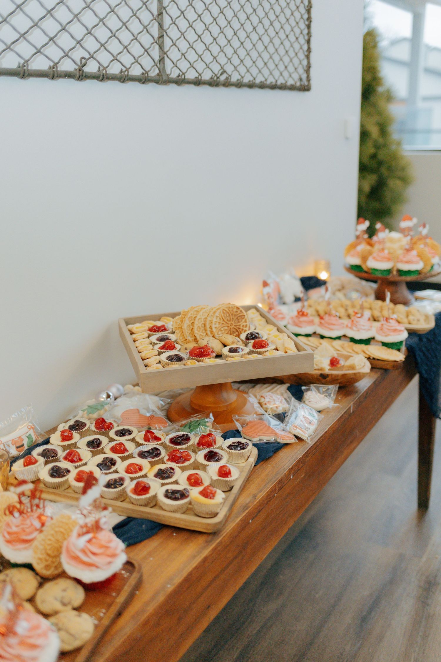 A wooden table displays an elegant holiday dessert spread with tarts, cupcakes, and assorted festive treats.