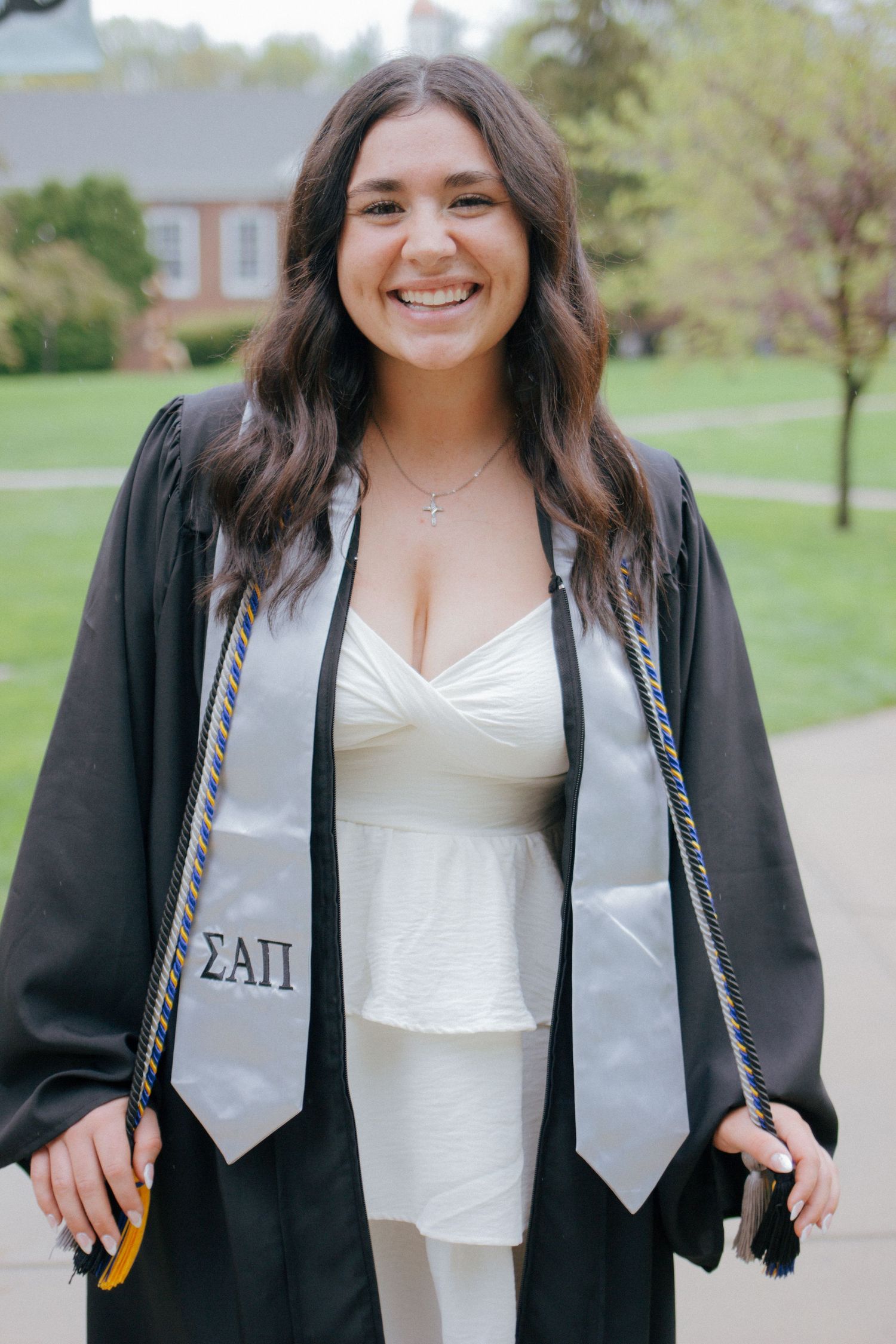 Smiling college graduate in black gown with Sigma Alpha Pi stole holding graduation tassel.