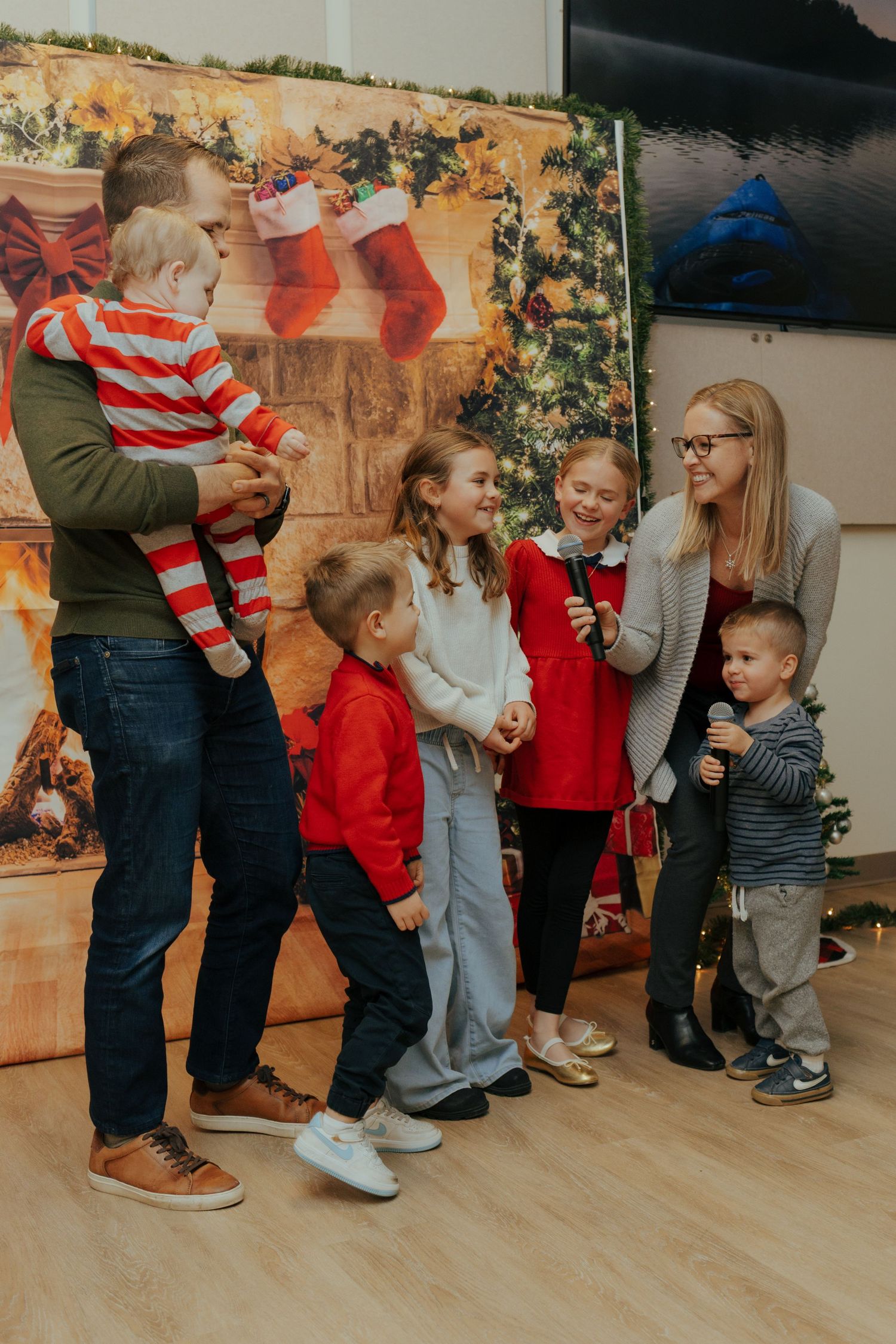 A family with young children in red holiday outfits poses together in front of a festive Christmas backdrop.