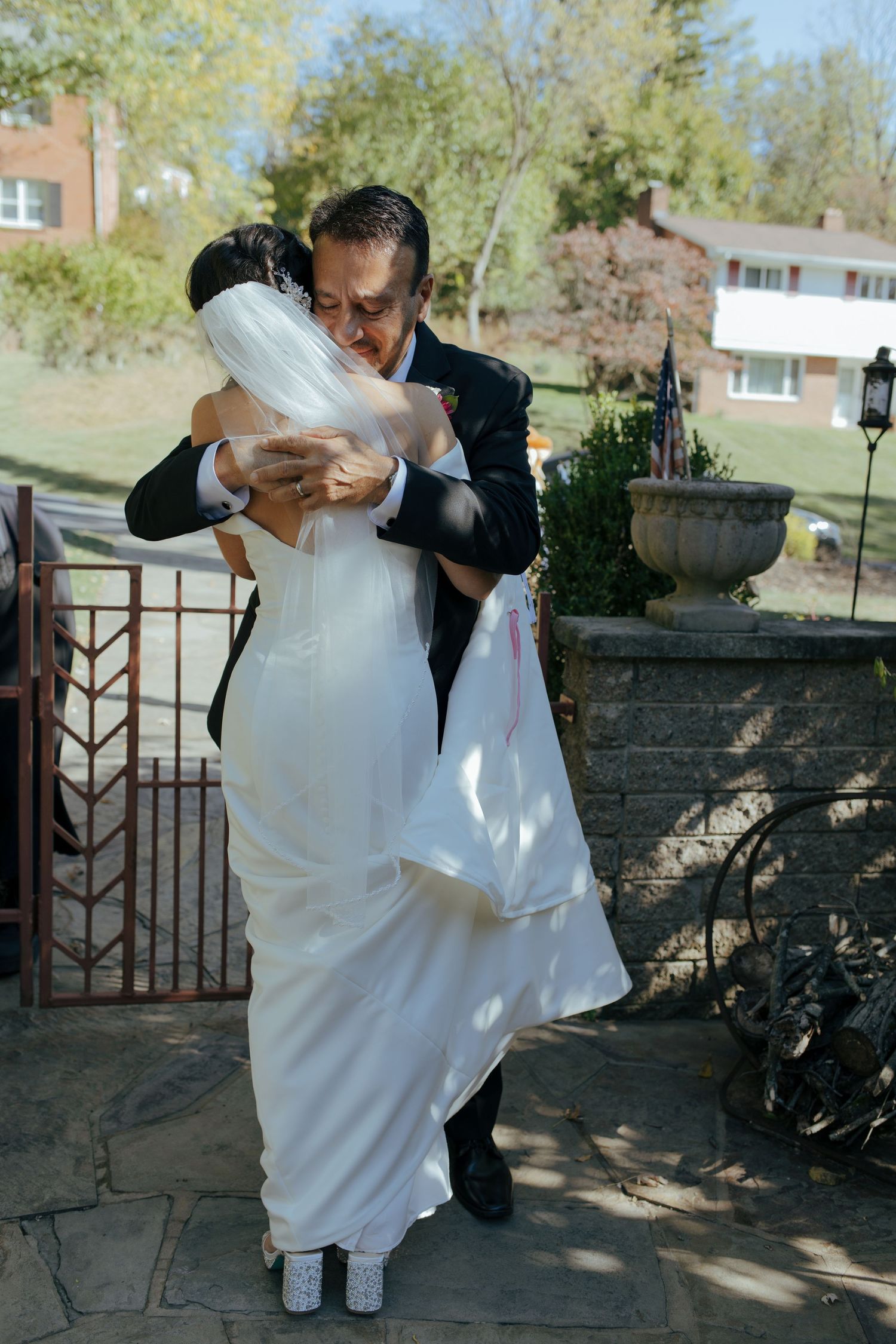 Groom lifts and embraces bride in white gown on stone patio during outdoor wedding day.