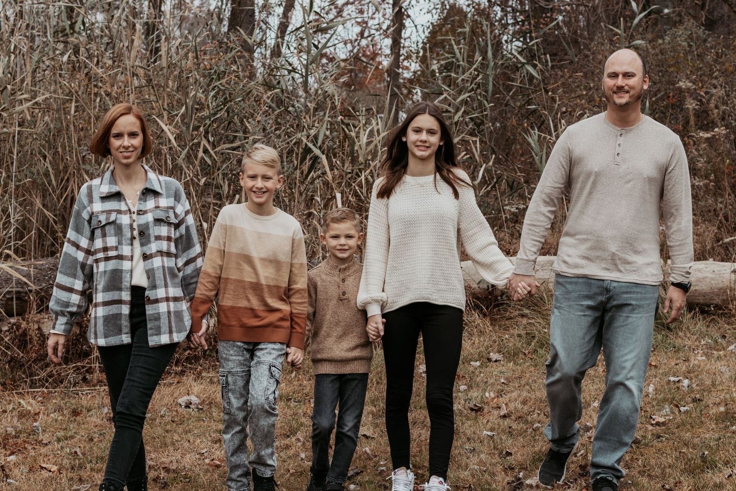 Family of five holding hands walking together in autumn woodland setting.