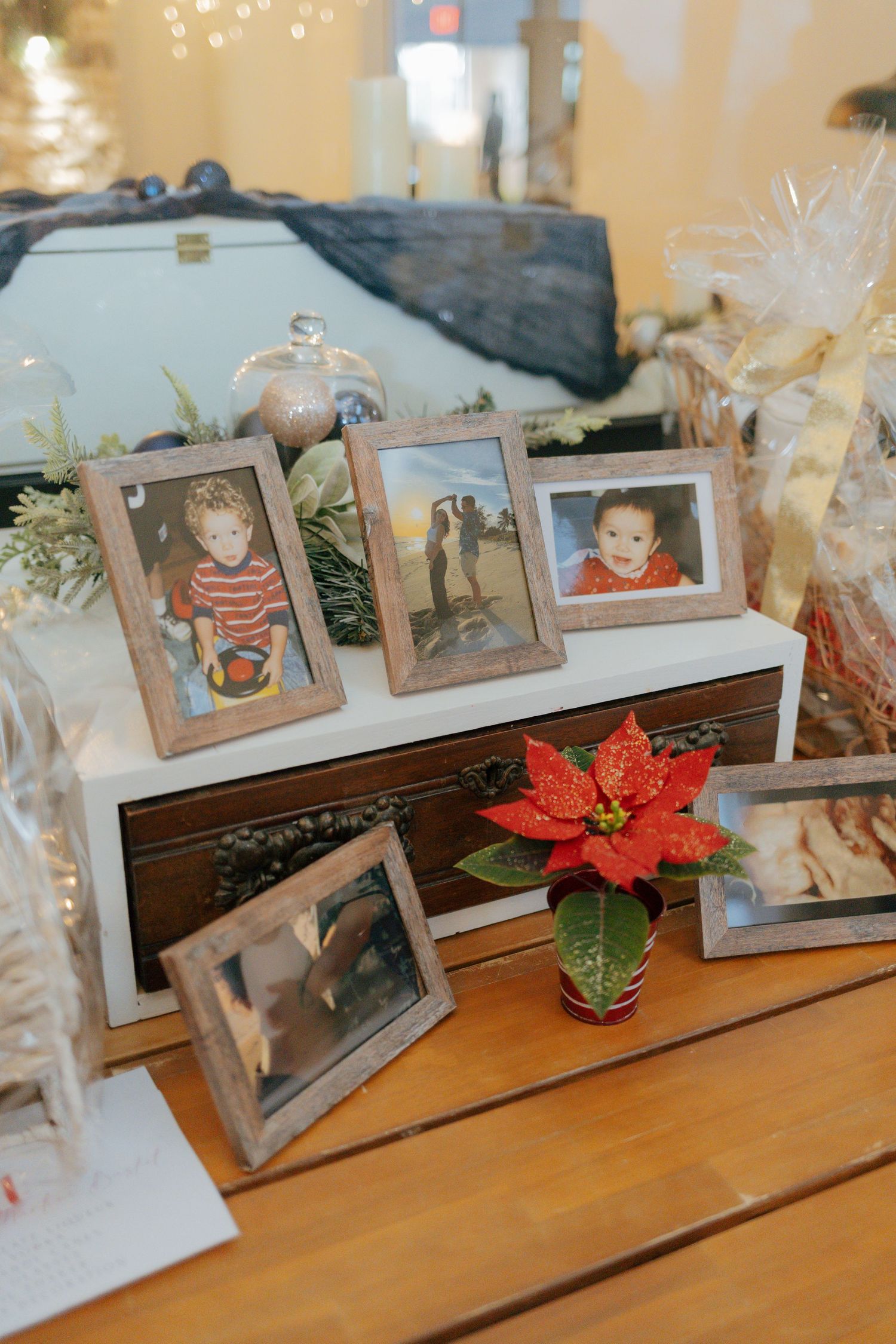 Framed family photos and a red poinsettia are displayed on a wooden table at a holiday baby shower.