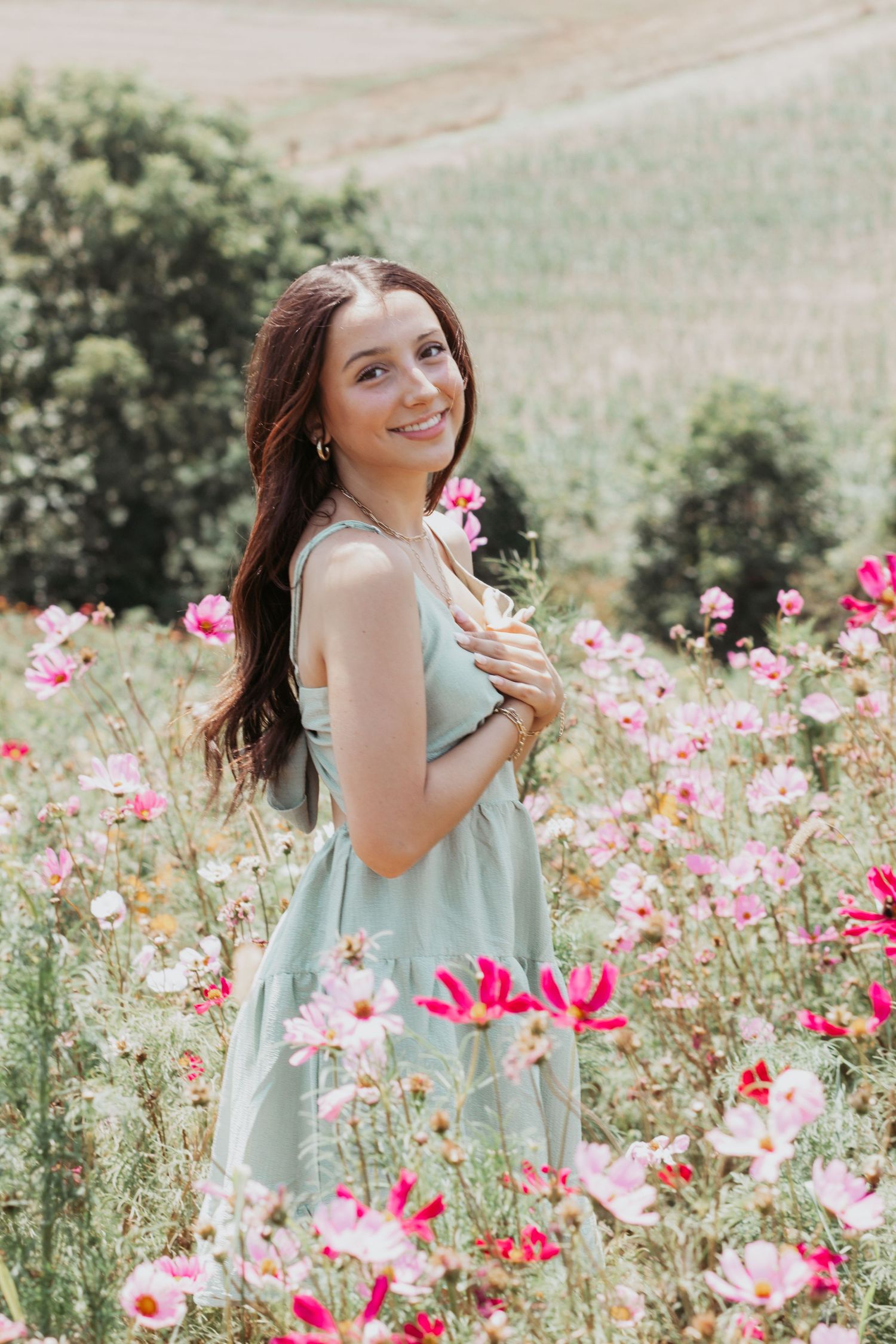 Young woman in mint dress smiling among pink cosmos flowers in a sunny field.