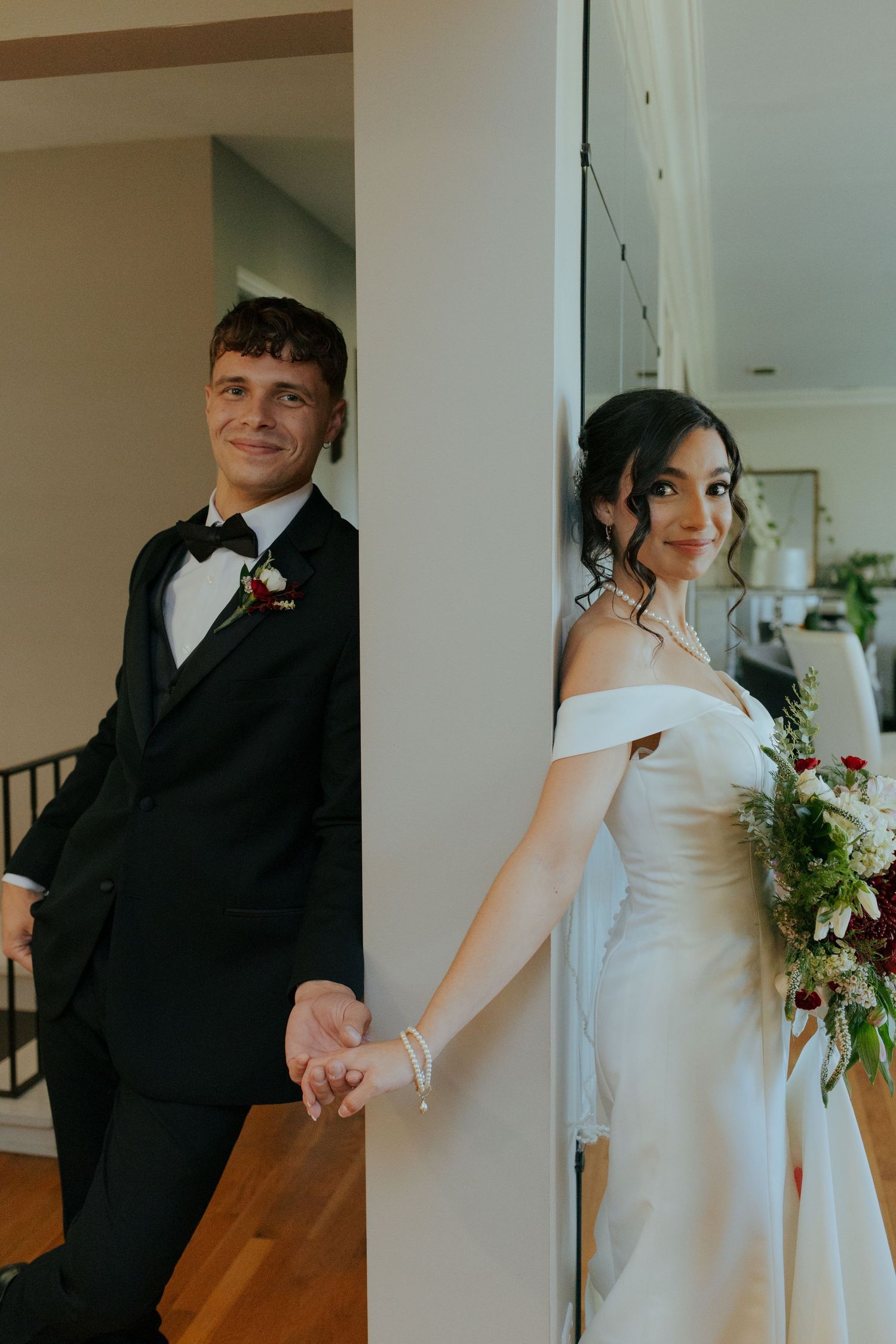 Bride and groom holding hands around a doorway, bride holding a lush floral bouquet.
