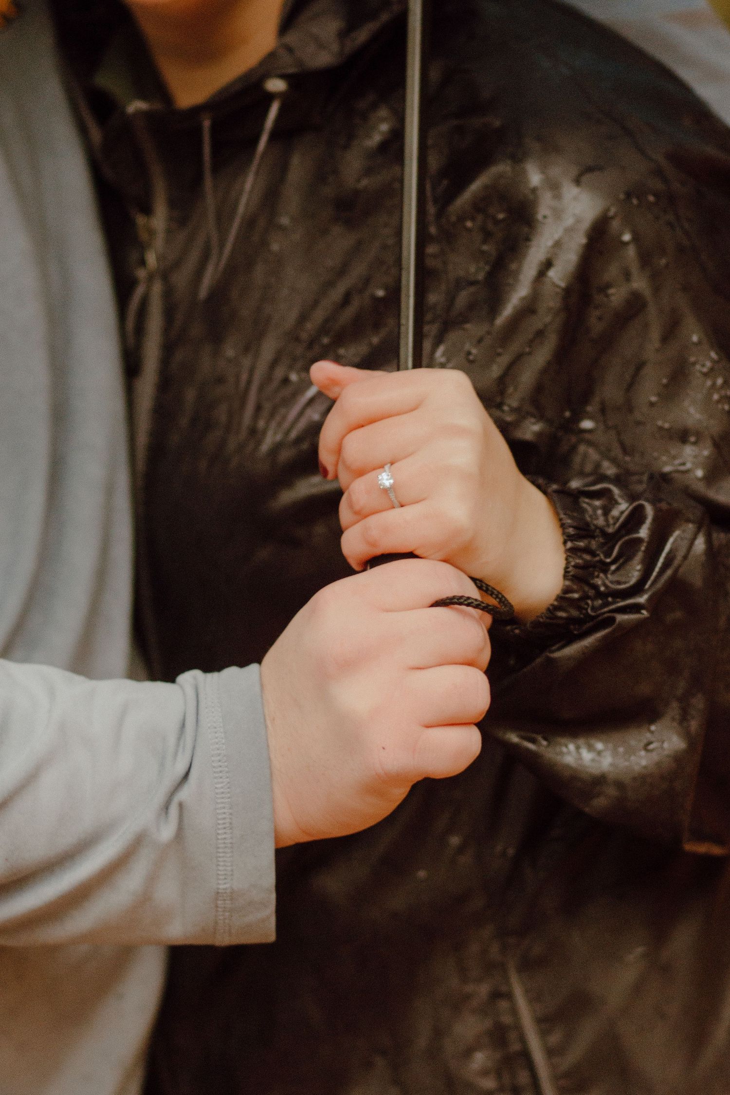 Couple holding an umbrella together in the rain, with an engagement ring visible on the woman's finger.