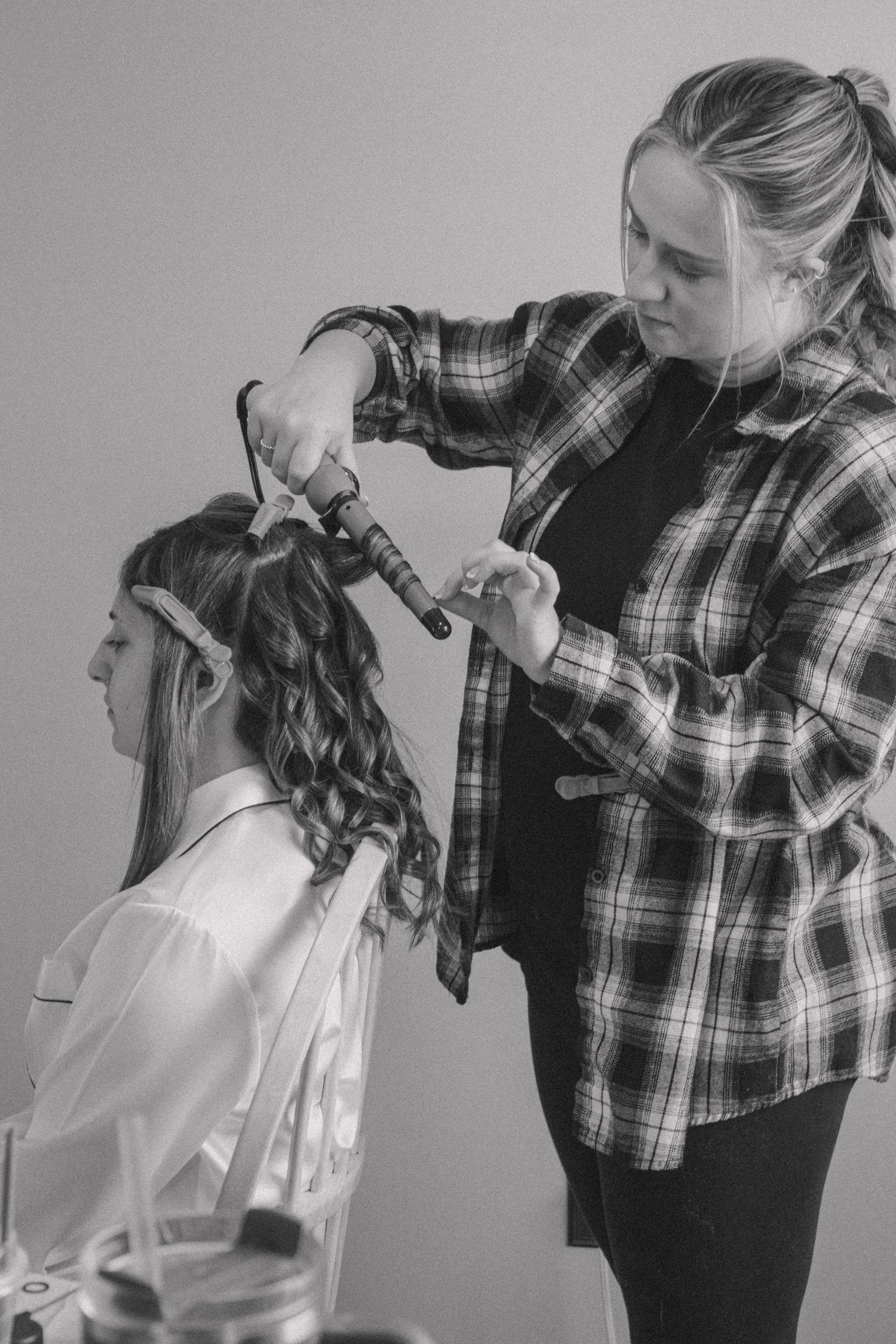 Black and white photo of hairstylist curling bride's hair during wedding preparation.