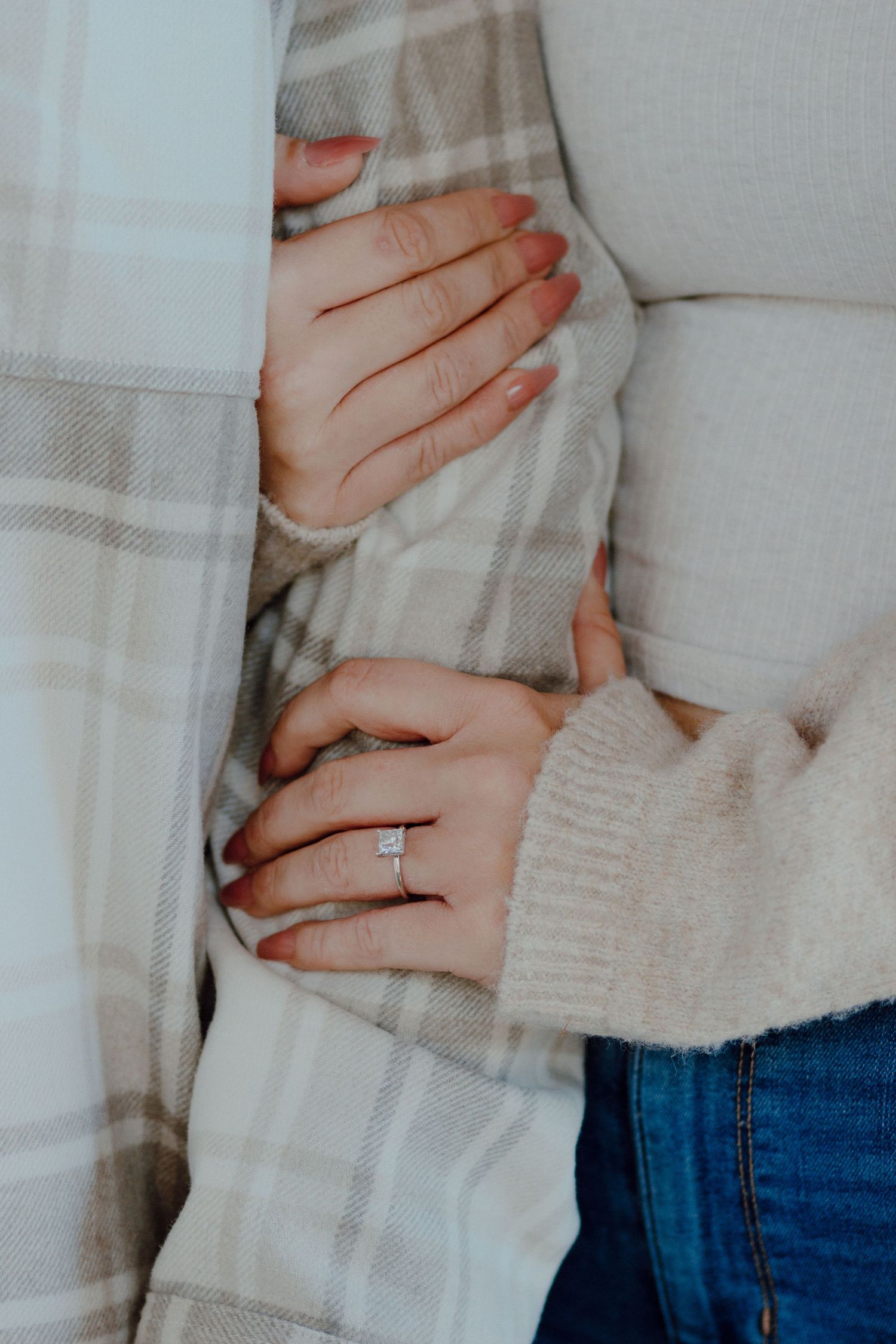 Close-up of a woman's hands showing a square diamond engagement ring while embracing her partner.