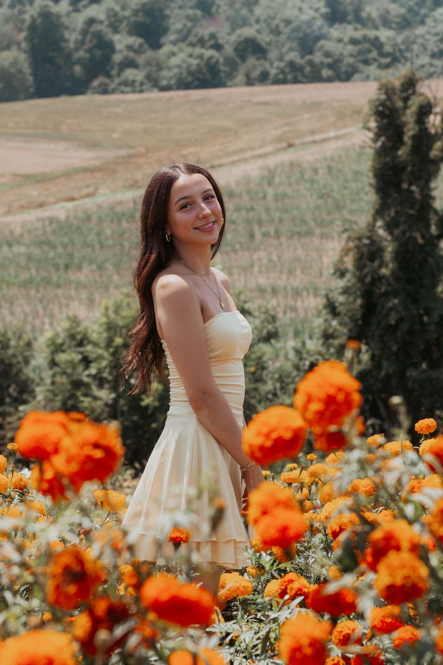 Young woman in white strapless dress smiling among vibrant orange marigold flowers in field.