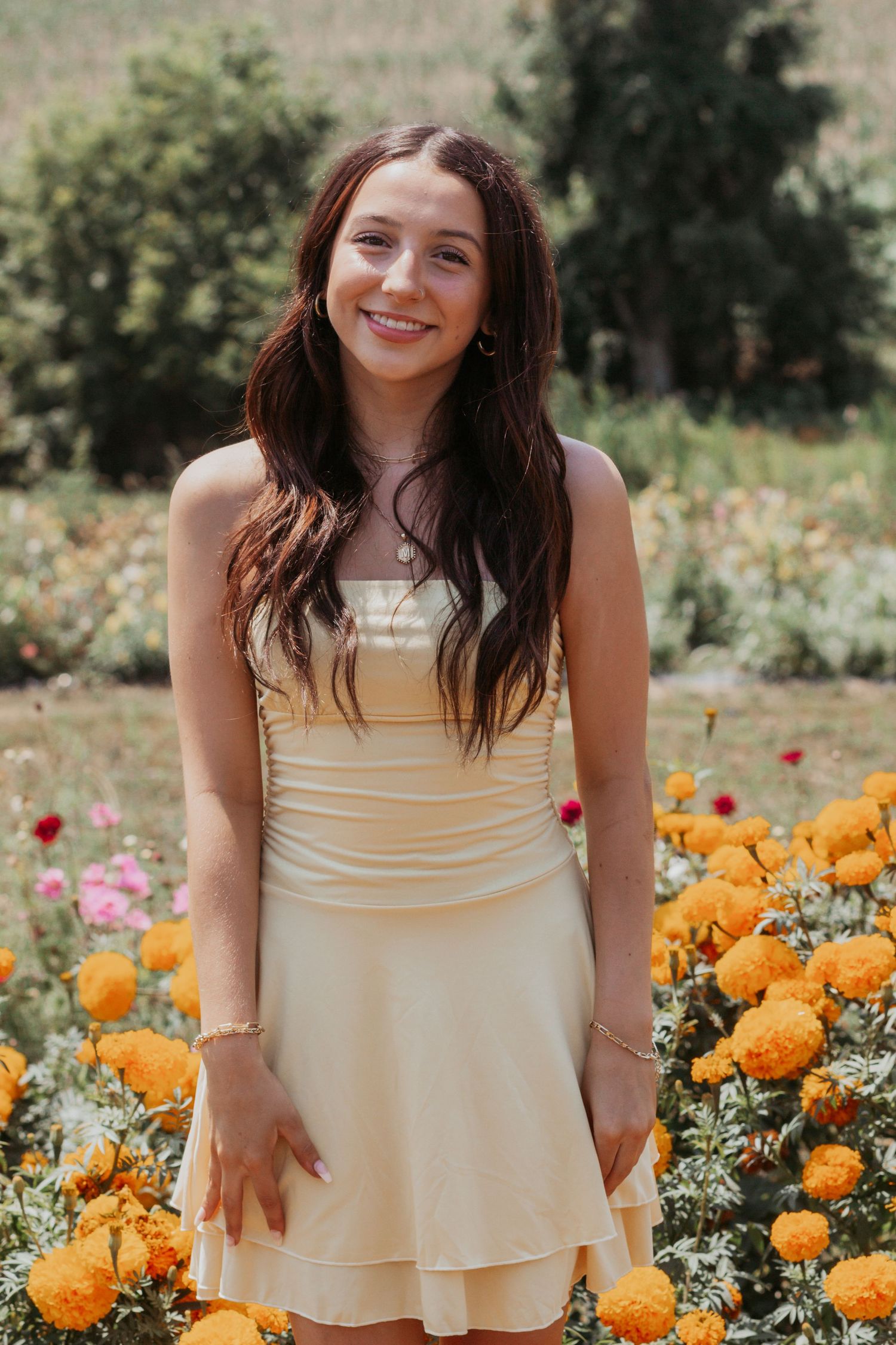 Smiling brunette teen in yellow dress posing among marigolds in a flower garden.