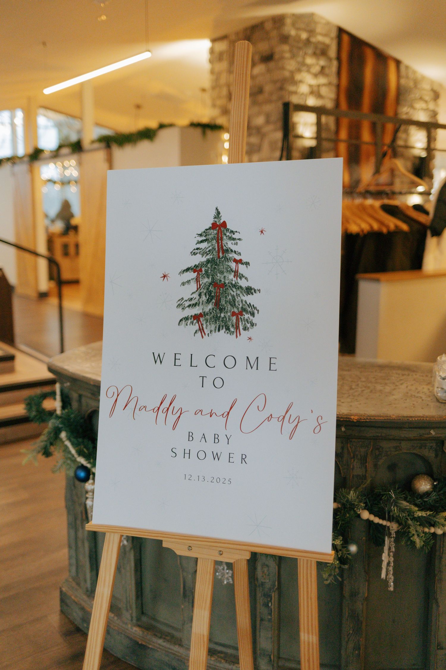 A welcome sign on an easel reads Welcome to Maddy and Cody's Baby Shower with a Christmas tree illustration.