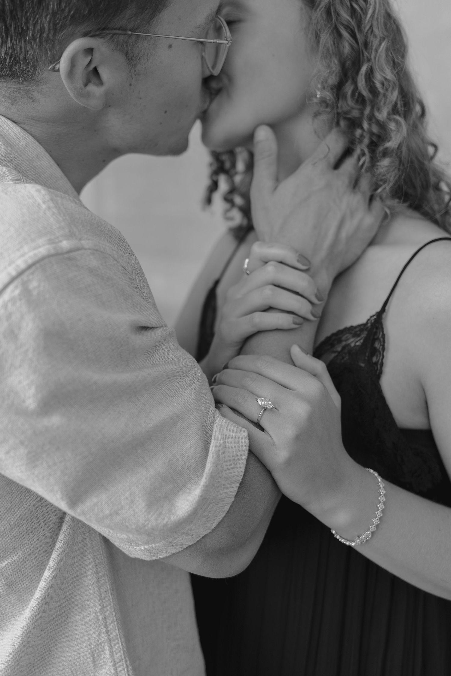 Black and white photo of an engaged couple holding hands, showcasing a diamond engagement ring and bracelet.