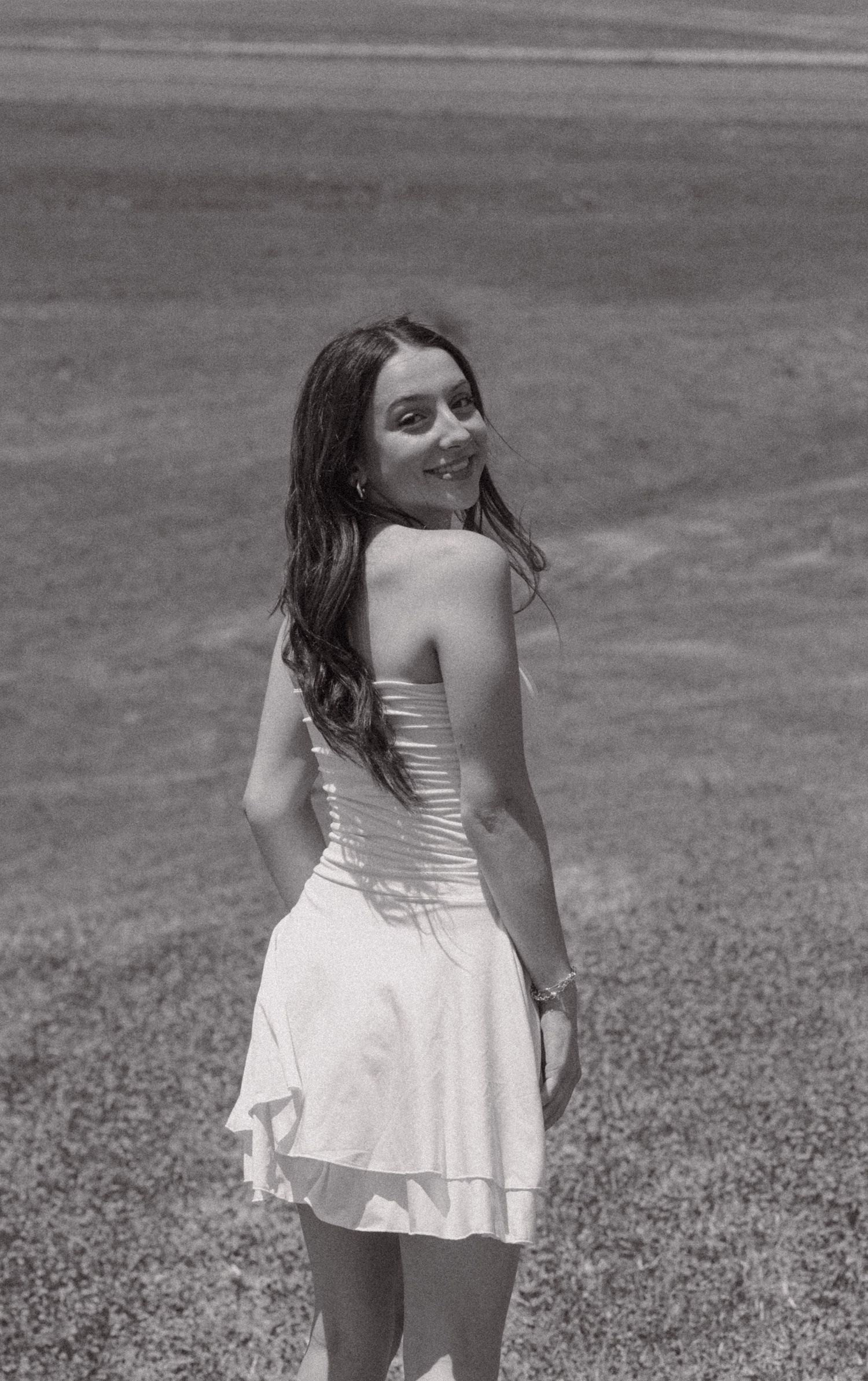 Black and white photo of a young woman in a white dress posing outdoors.